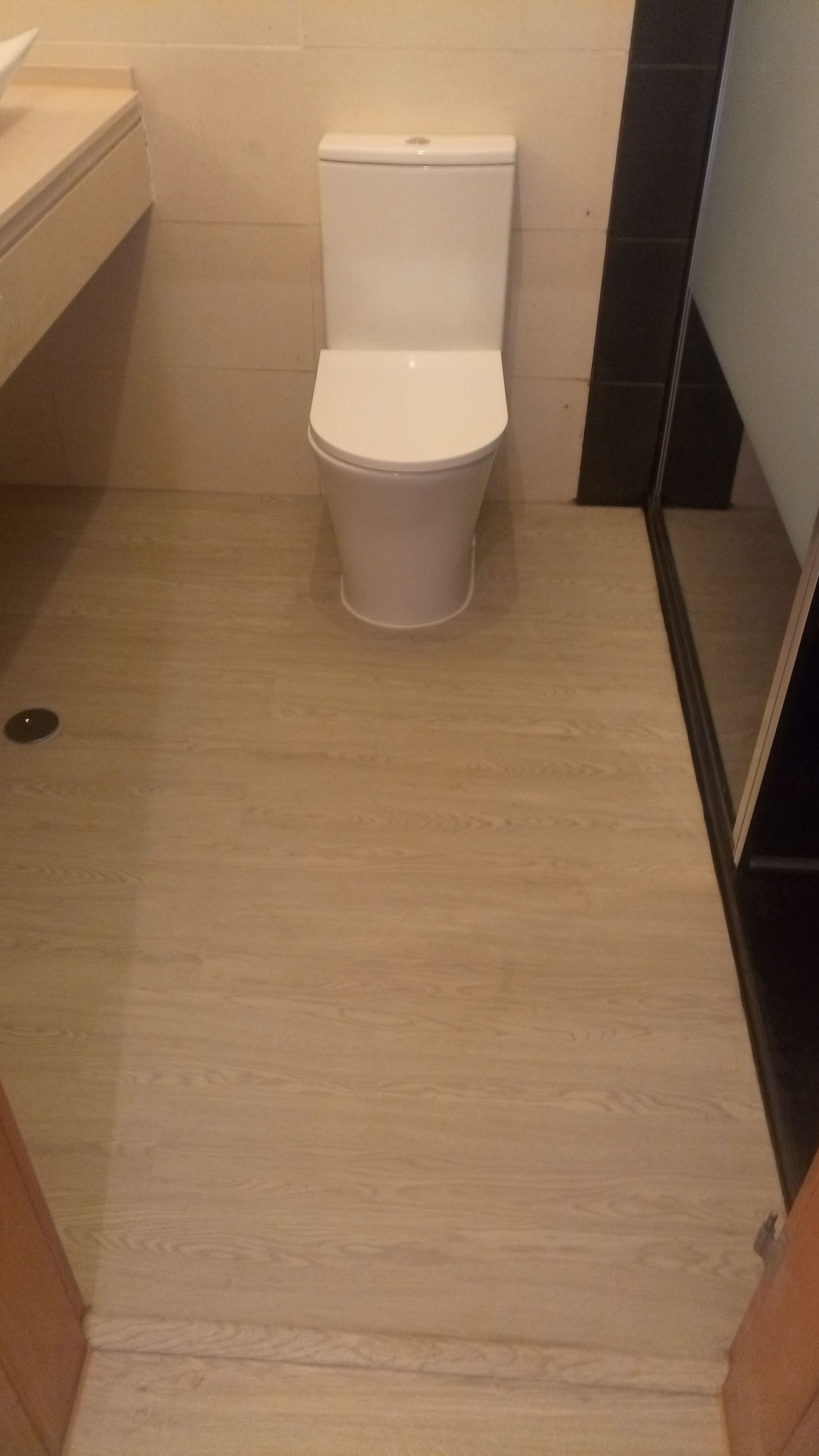 Um vaso sanitário centralizado em um banheiro com piso de azulejo claro e uma faixa vertical escura.