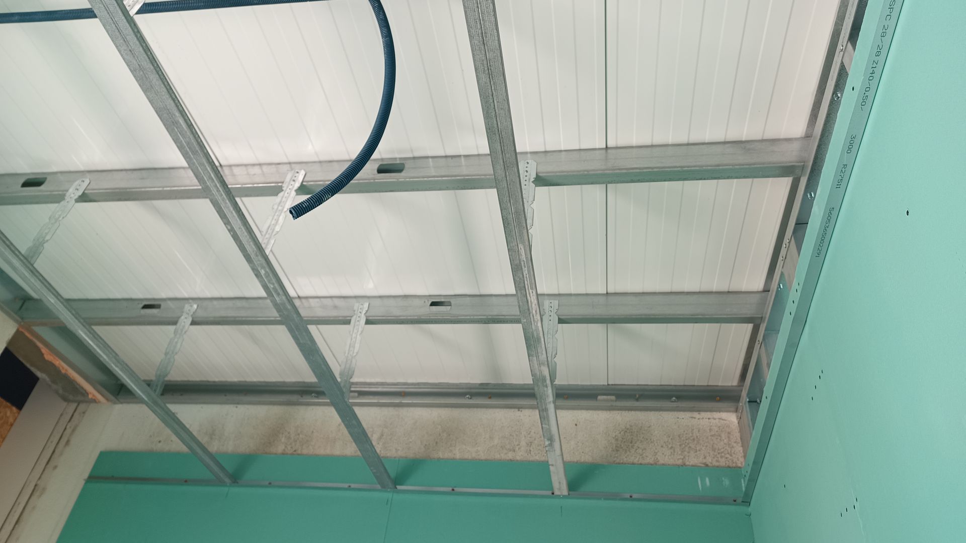 Estrutura metálica no teto com isolamento, fiação elétrica e uma parede verde-clara.