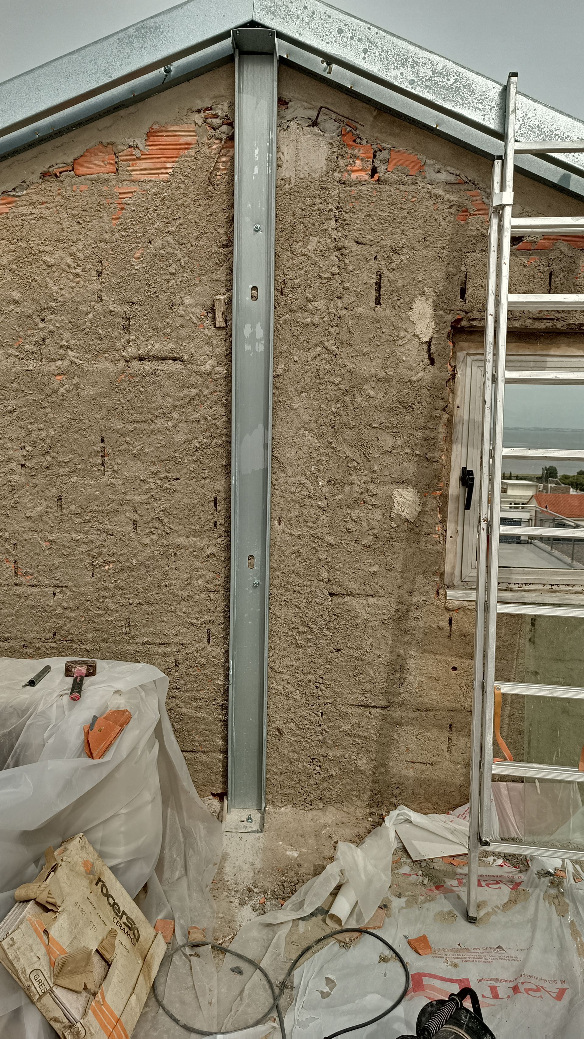 Viga metálica vertical instalada em uma parede texturizada e desgastada durante a construção. Escada encostada na parede.