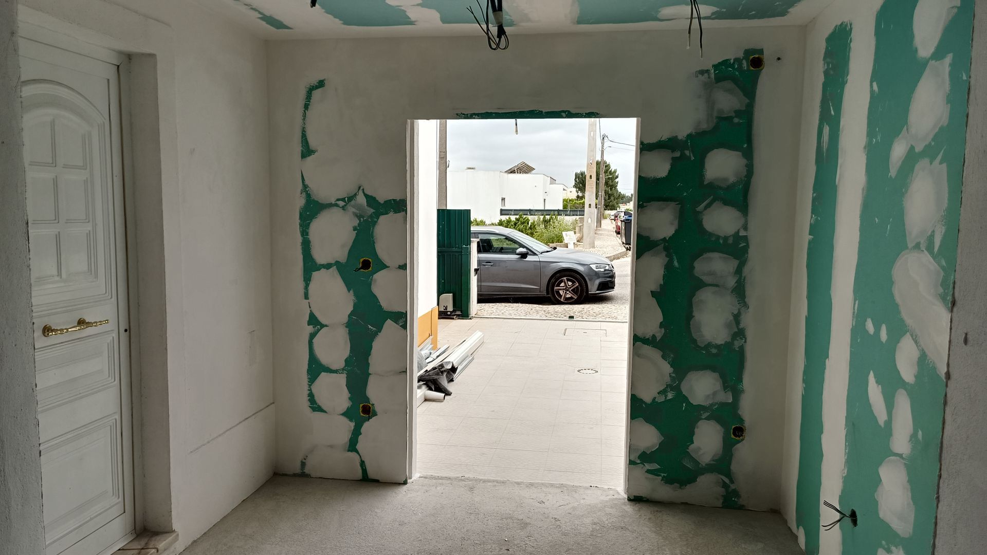 Vista interna de um cômodo em construção com porta de acesso ao exterior. Paredes de gesso verde visíveis.