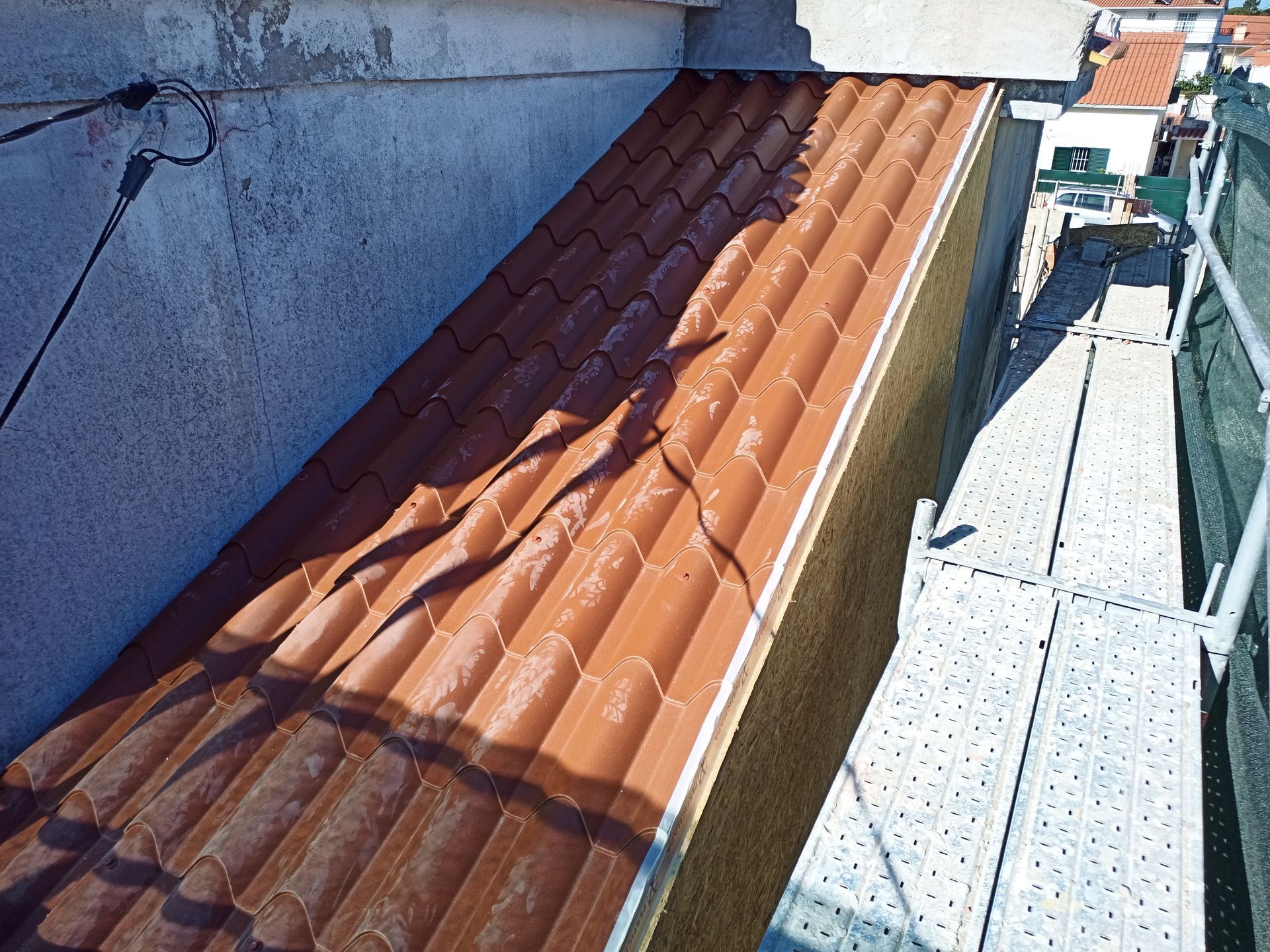 Seção do telhado de telhas com incidência direta do sol, ao lado de uma parede. Andaimes visíveis à direita.