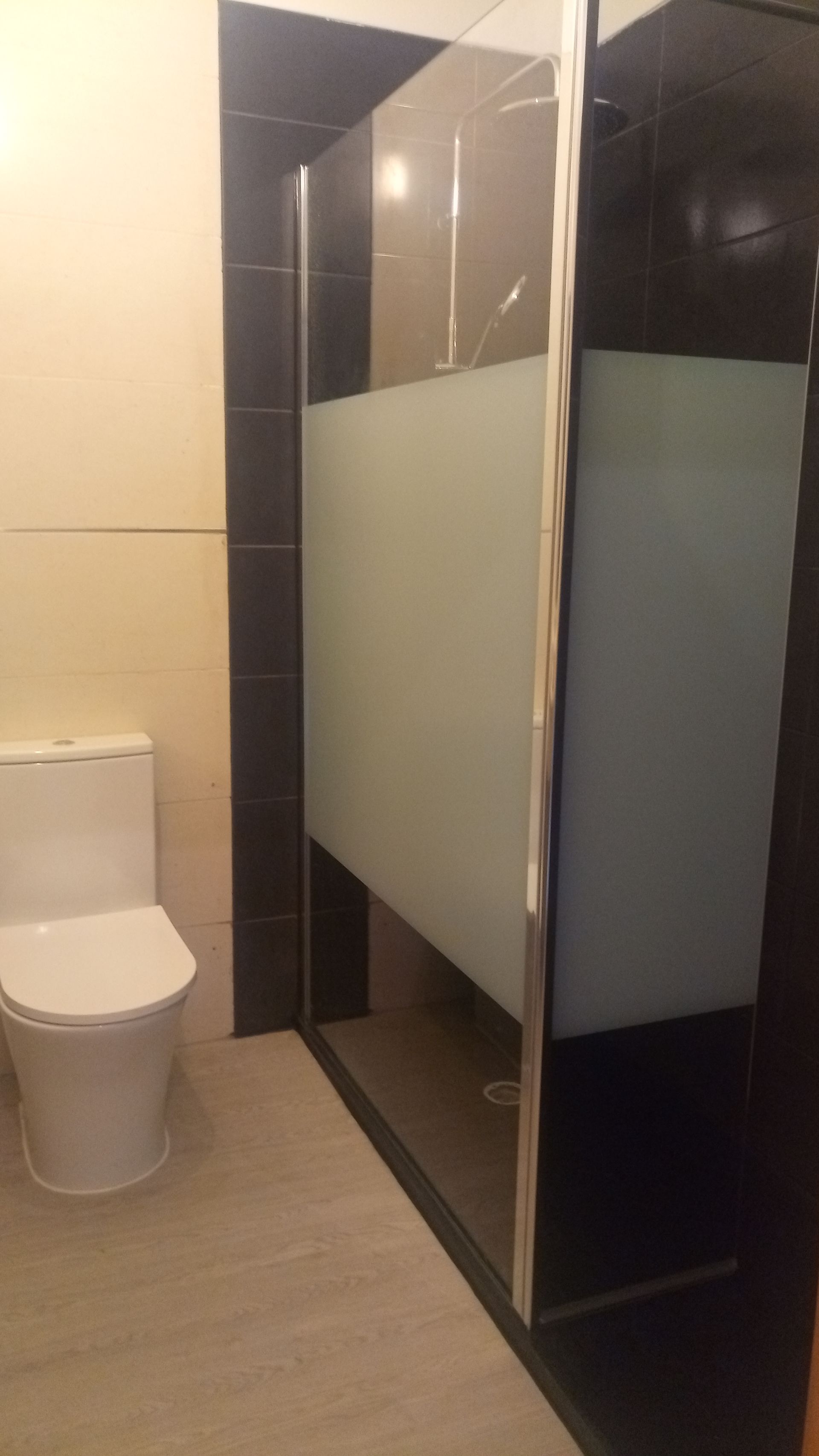 Um banheiro com vaso sanitário branco e box de chuveiro com vidro fosco e acabamento preto.