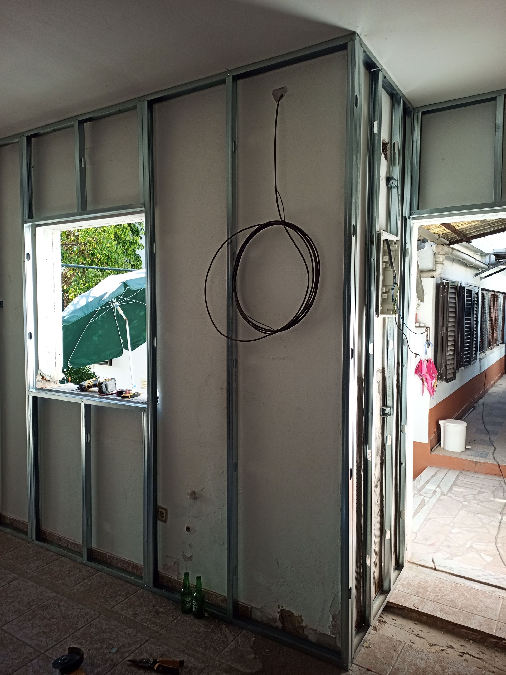 Estrutura de parede interna com perfis metálicos, uma janela e uma porta. Obra em andamento.