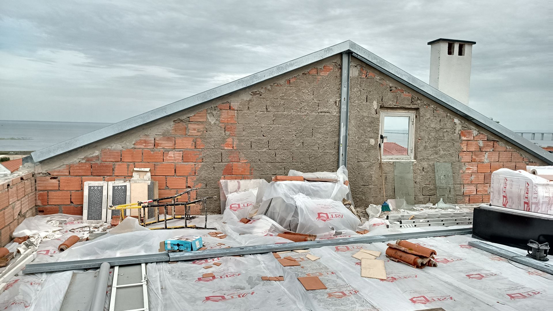 Construção do telhado com tijolos aparentes, concreto desgastado e céu nublado.