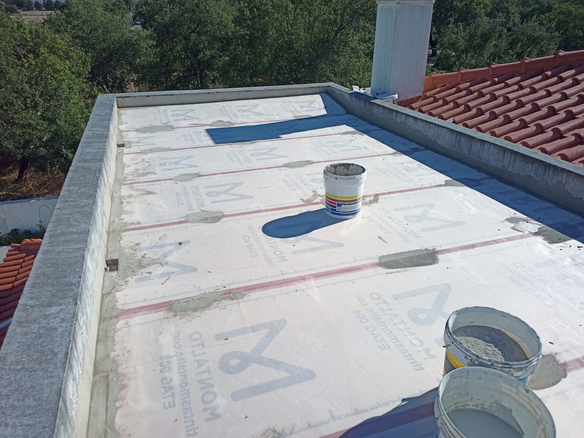 Telhado plano em construção com baldes de materiais; chaminé de tijolos ao fundo.