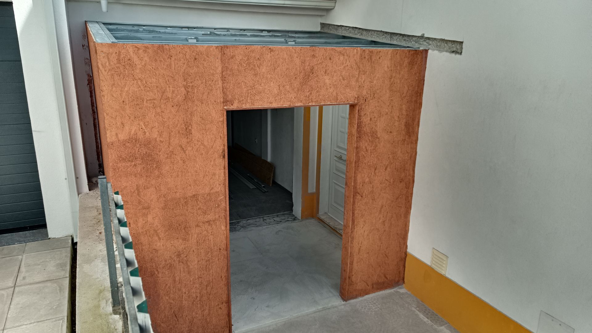 Uma porta com moldura texturizada marrom e um telhado simples, situada em uma varanda.