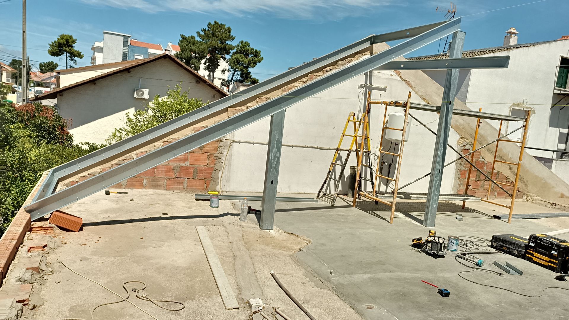 Estrutura de montagem de painéis solares sendo instalada em um telhado, com andaimes e edifícios ao fundo.