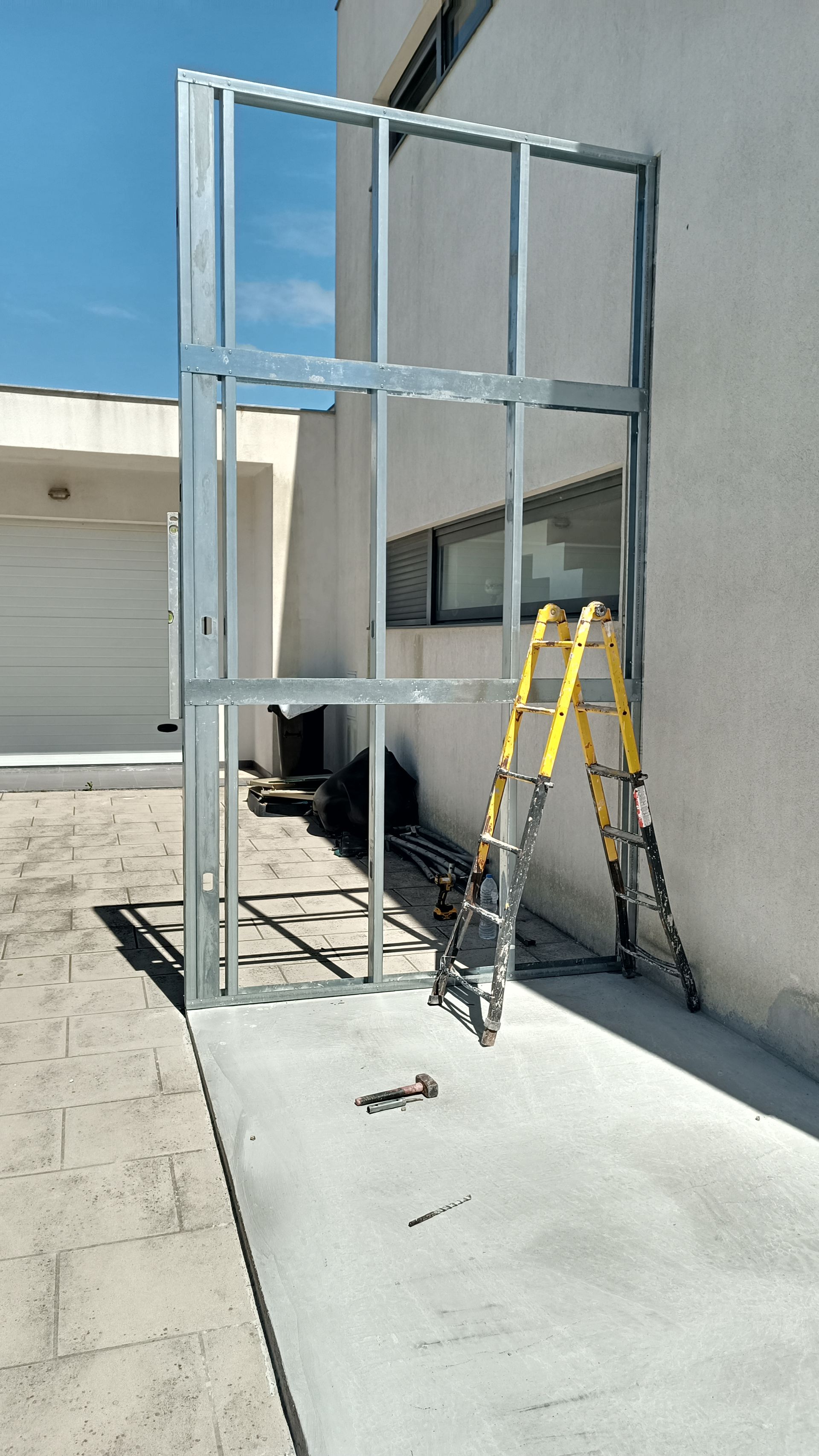 Estrutura metálica contra um prédio branco com uma escada amarela encostada em uma superfície de concreto.