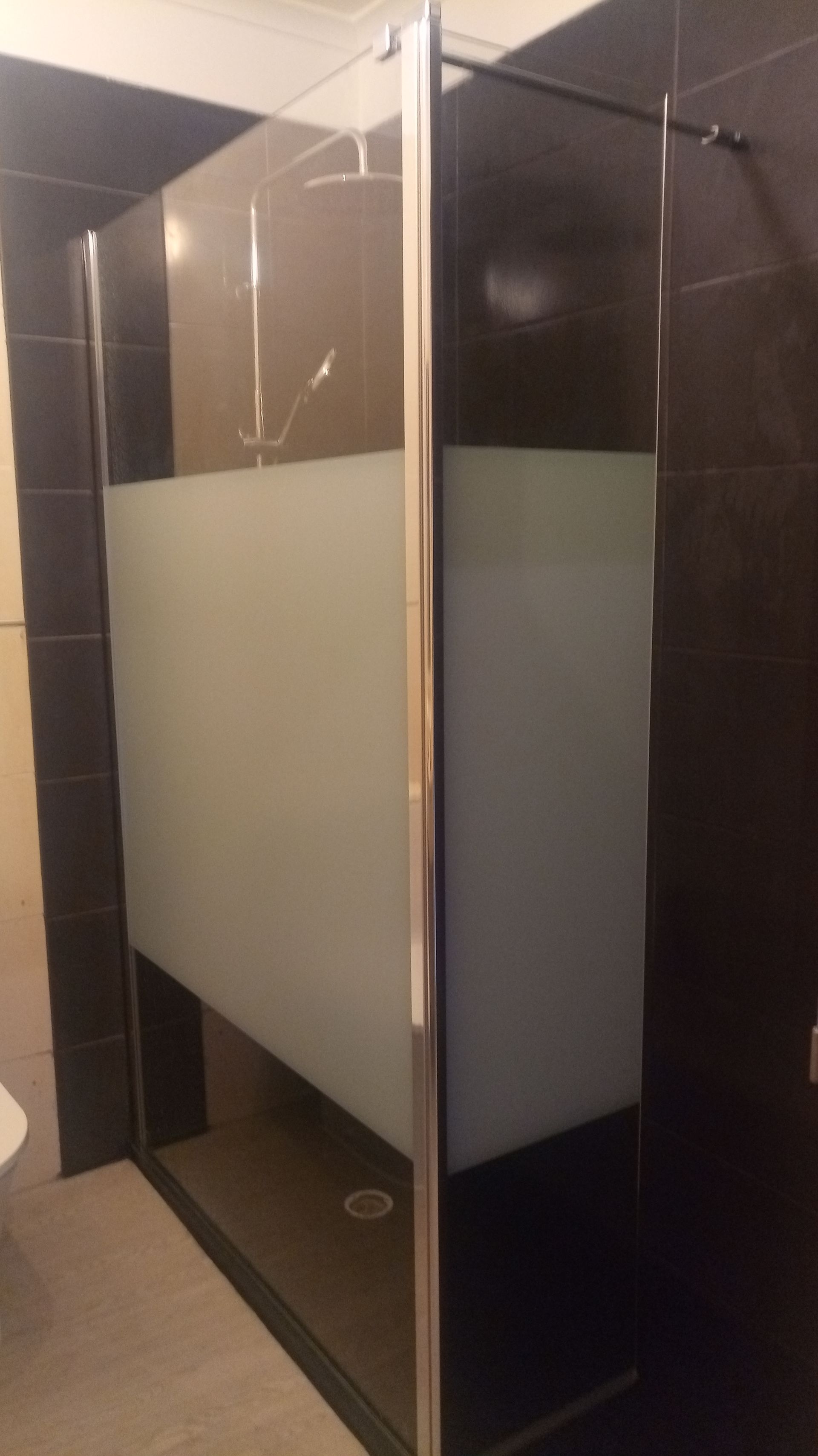 Cabine de duche com vidro fosco e paredes revestidas a azulejos pretos.