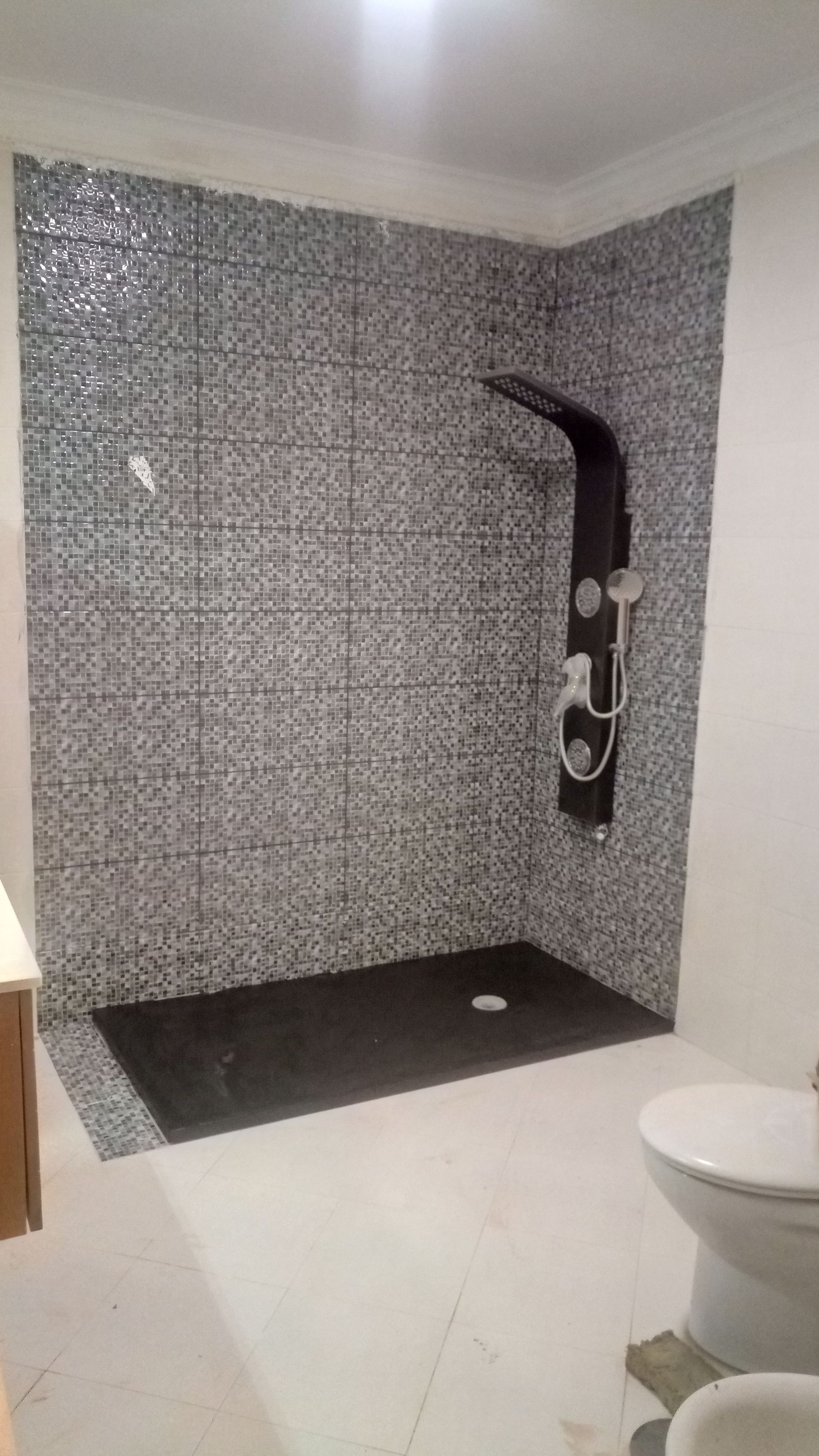 Banheiro com paredes do box revestidas com azulejos pretos, base do box preta e piso de azulejo branco.