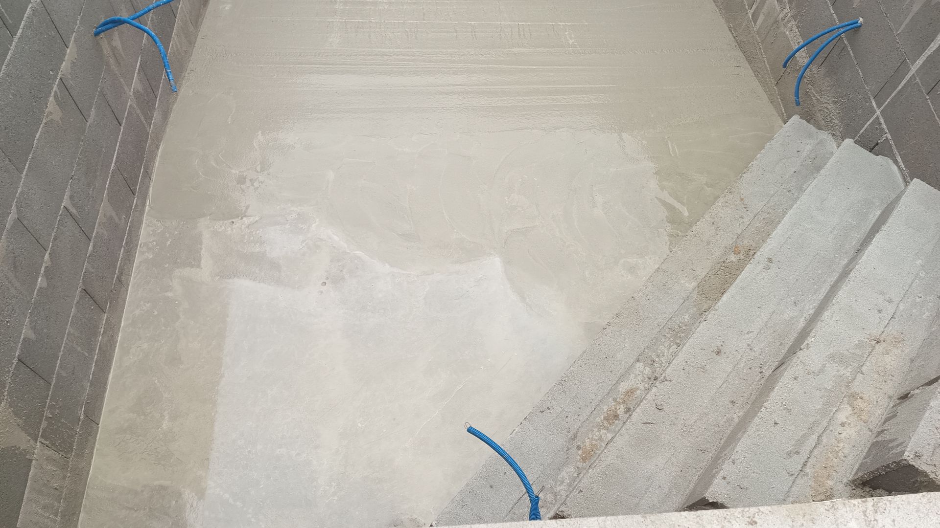 Vista interior de uma construção de concreto, com escadas, apresentando uma superfície irregular de cor clara.