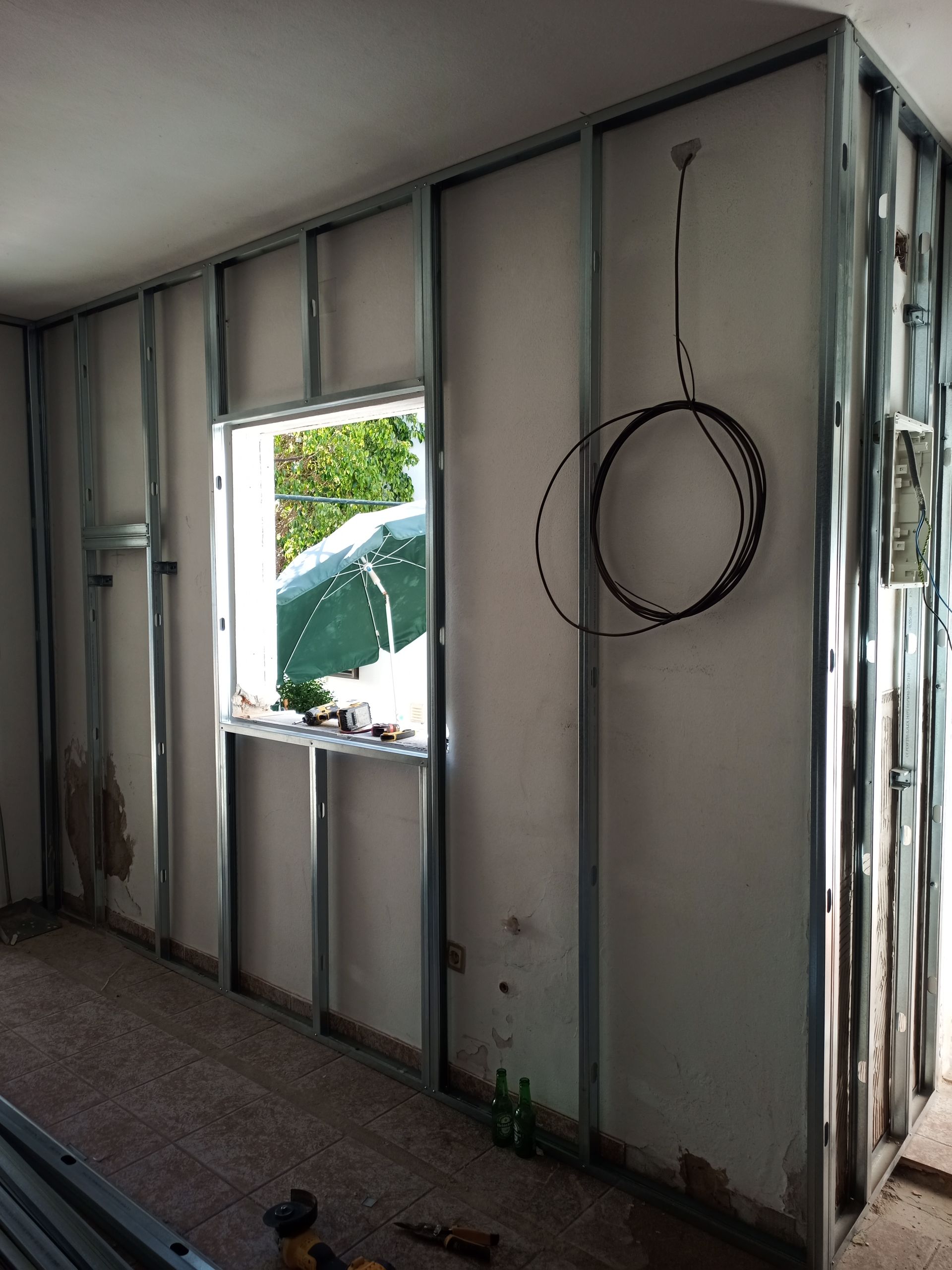 Estruturas metálicas delimitam um cômodo com janela. A fiação elétrica está instalada. Parte das paredes de gesso acartonado está instalada.