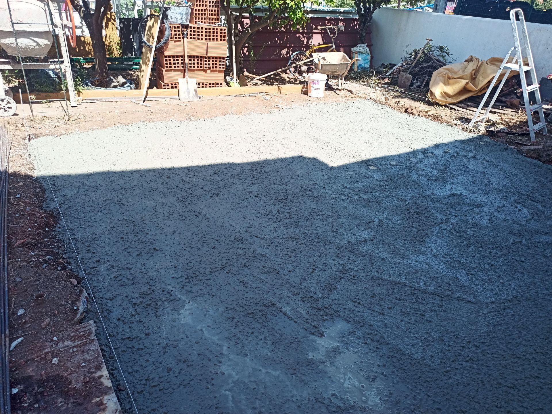 Pátio de concreto recém-construído, canteiro de obras, cercado por ferramentas e materiais.