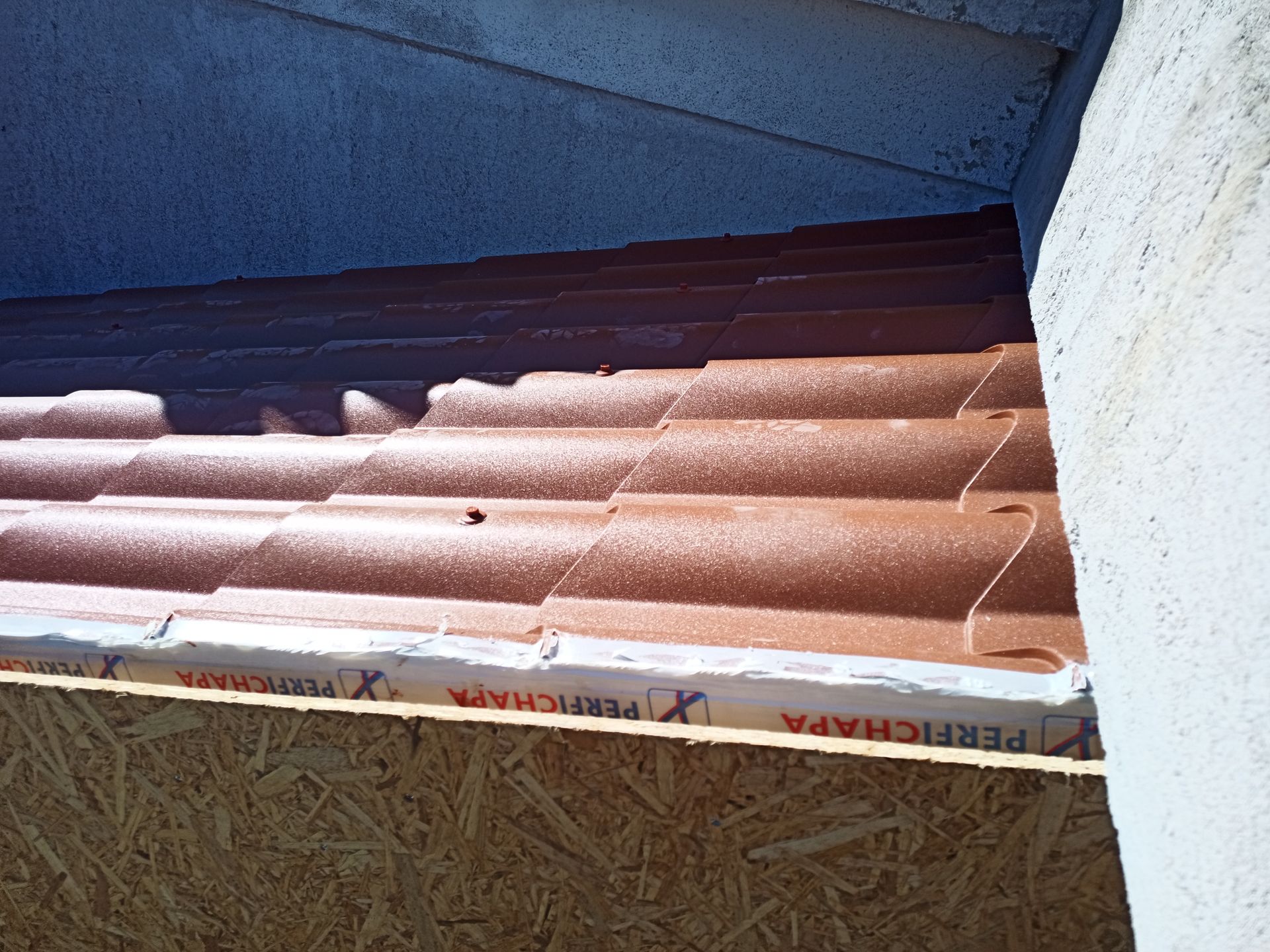 Detalhe de telhas marrons ao lado de uma parede de estuque de cor clara e uma estrutura de madeira.