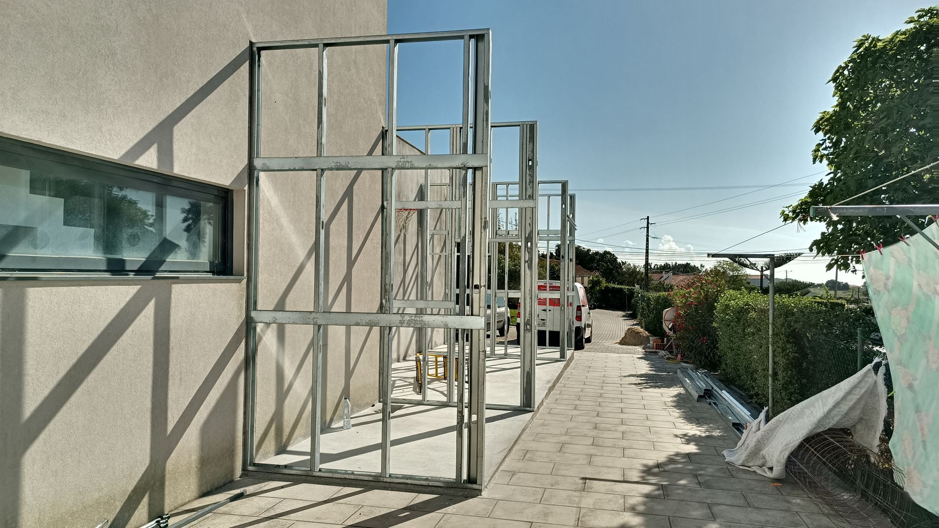 Estrutura metálica ao lado de um edifício. Caminho e folhagem ao fundo, sob um céu ensolarado.