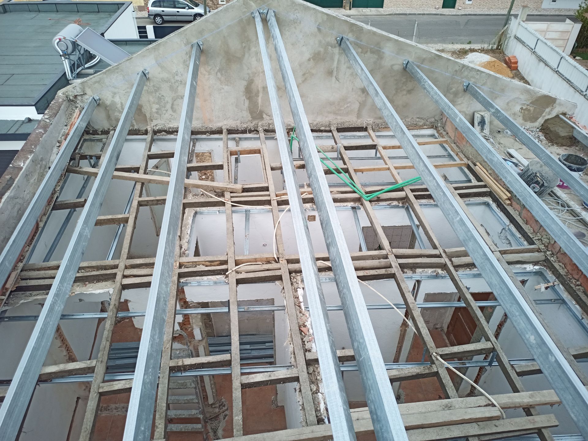 Vista aérea de um telhado em construção; vigas de madeira e suportes metálicos expostos.