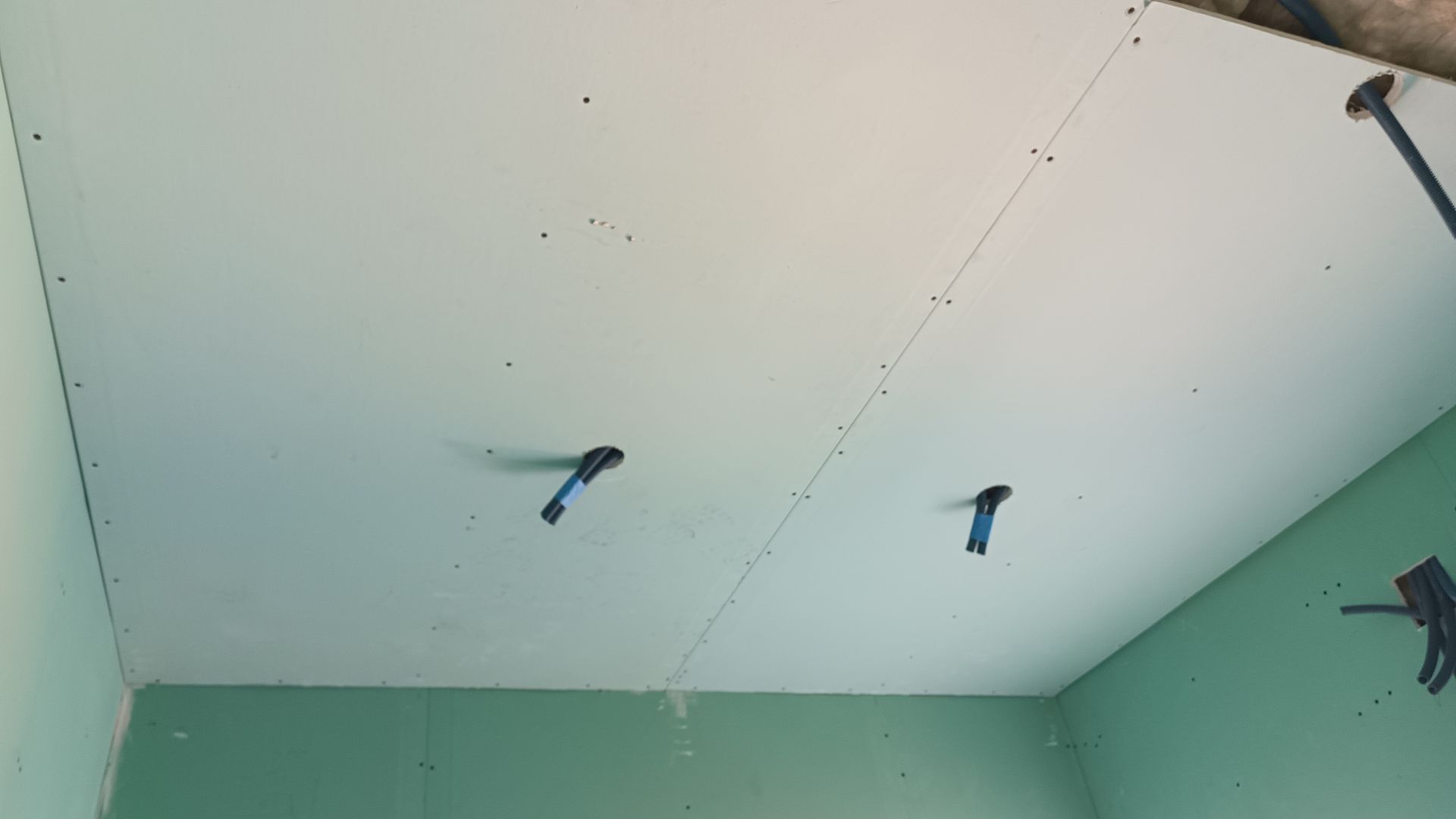 Teto de gesso branco com dois fios azuis saindo dele, paredes verdes.