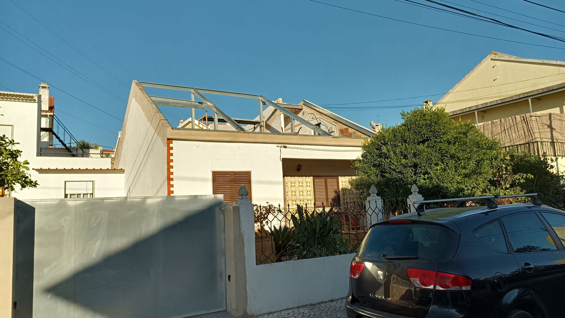Casa com estrutura de telhado aparente, carro estacionado em frente, céu azul claro.