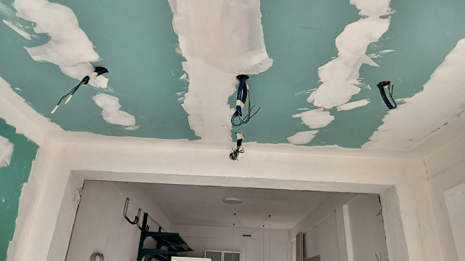 Teto com fiação e drywall expostos durante a reforma. Predominam as cores azul claro e branco.