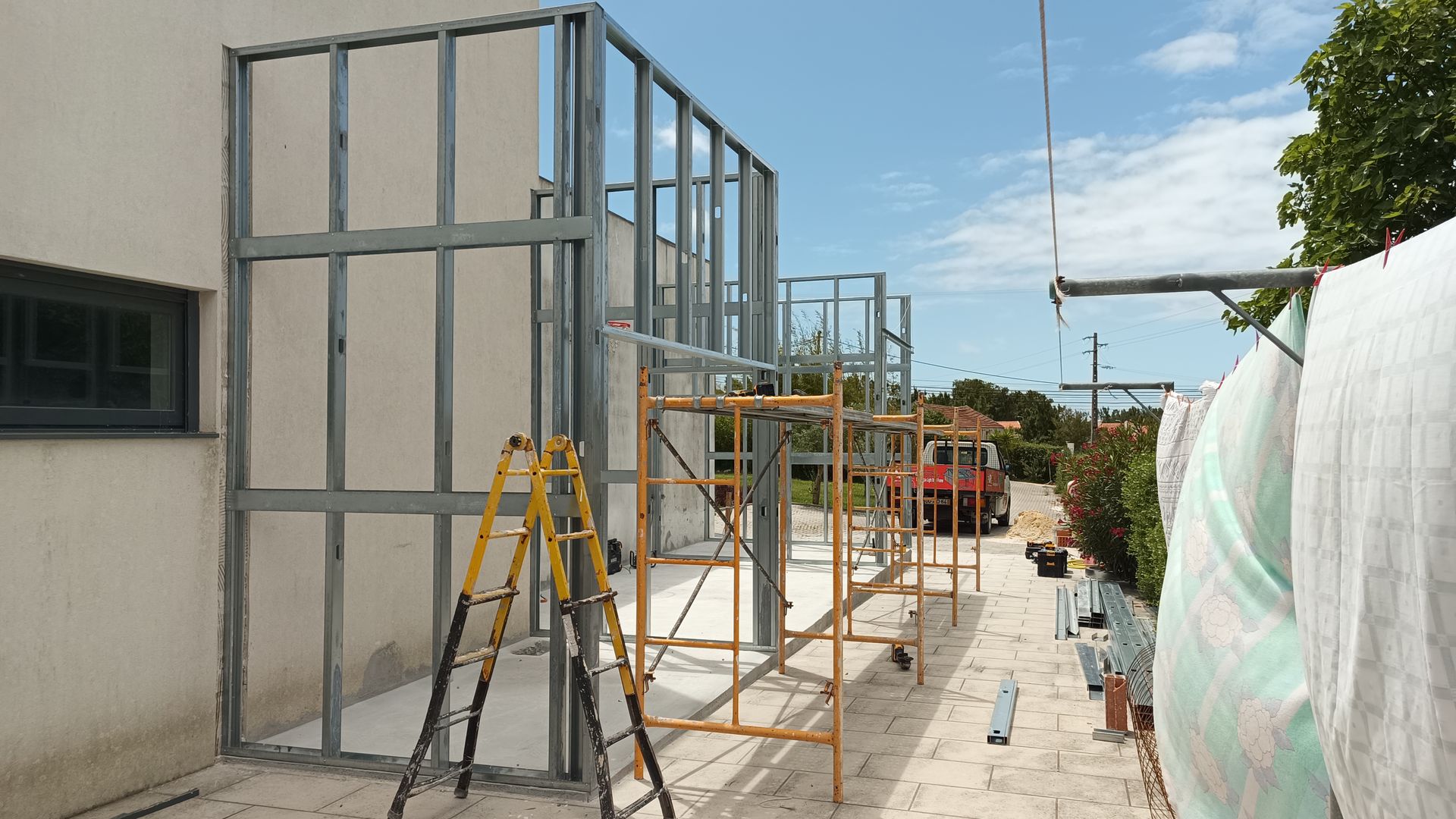 Estrutura metálica da fachada de um edifício, com andaimes, junto a uma parede.