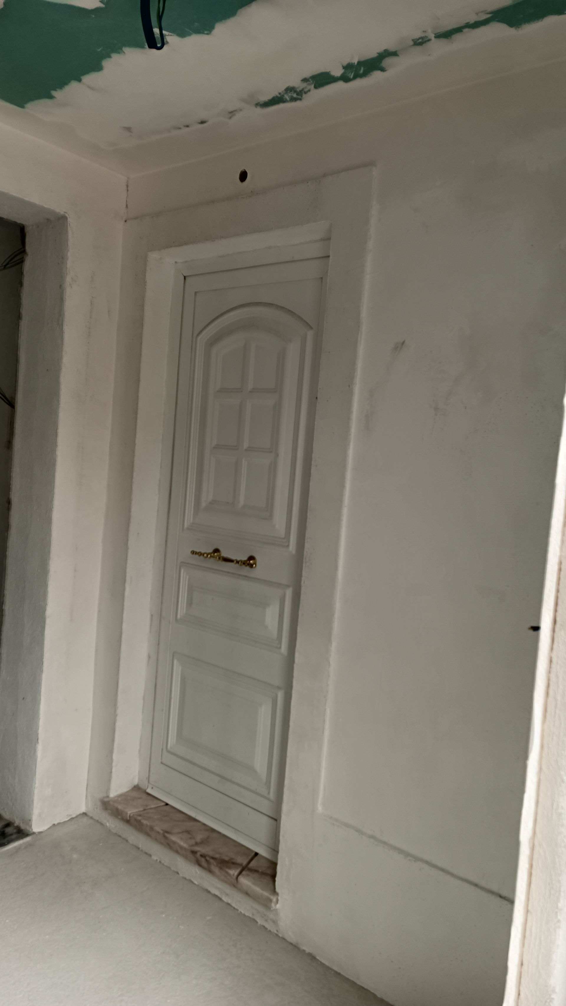 Porta branca com detalhes em painel em uma entrada com moldura branca; canteiro de obras.