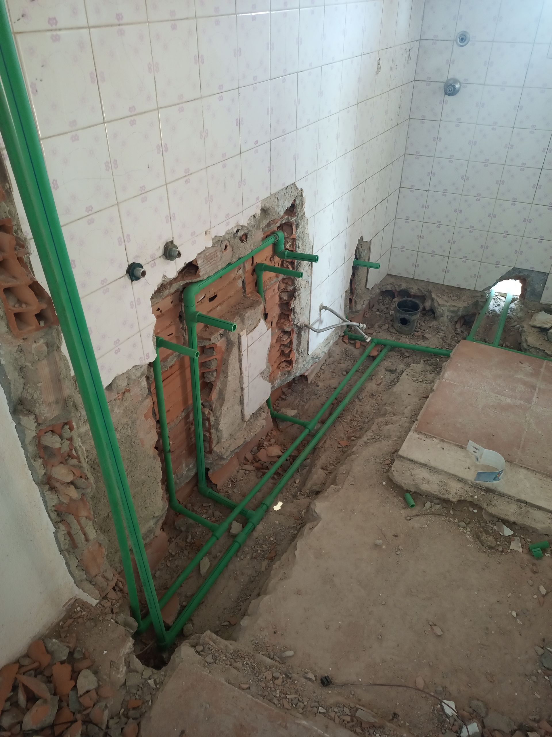 Tubos de encanamento verdes instalados na parede de um banheiro durante uma reforma.