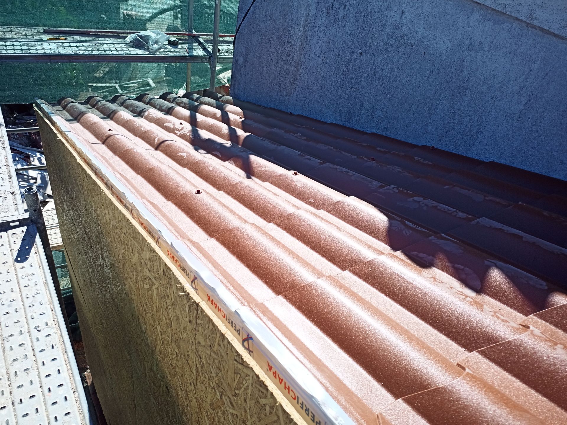 Telhado parcialmente coberto com telhas onduladas vermelhas, cenário de canteiro de obras.