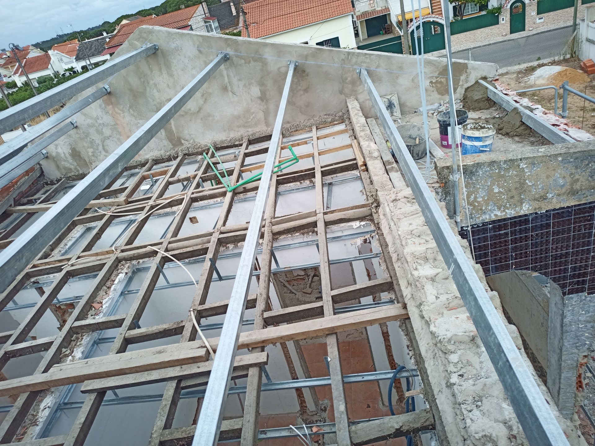 Canteiro de obras: vigas de madeira expostas, suportes metálicos e paredes de tijolos em um telhado em construção.