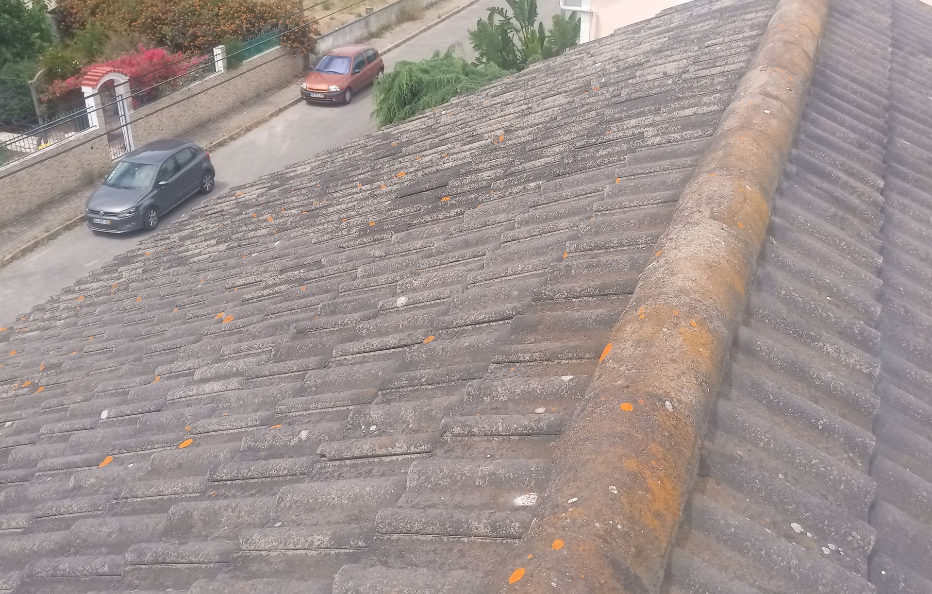 Vista aérea de um telhado desgastado, com uma cumeeira, uma estrada e dois carros visíveis abaixo.