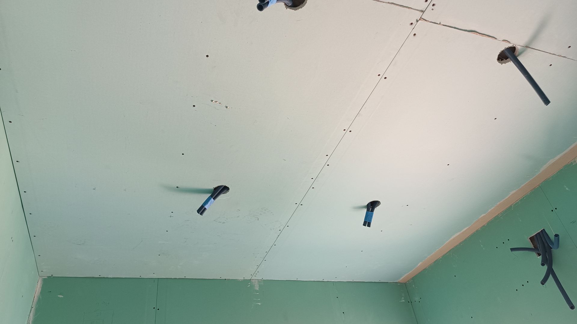 Teto com drywall e suportes de drywall azuis, alguns com fiação. Parede verde no canto.