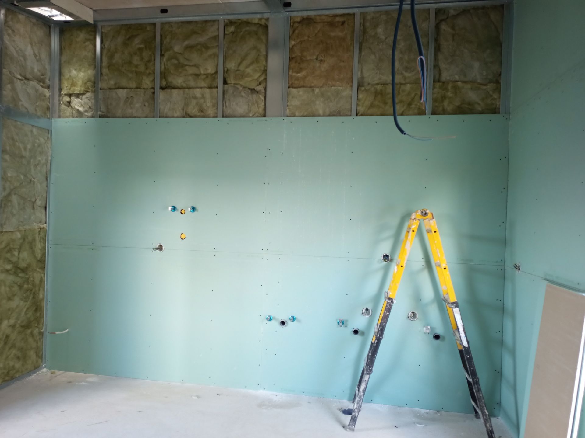 Construção interna: Paredes de gesso verde com acessórios de encanamento, isolamento e escada amarela.