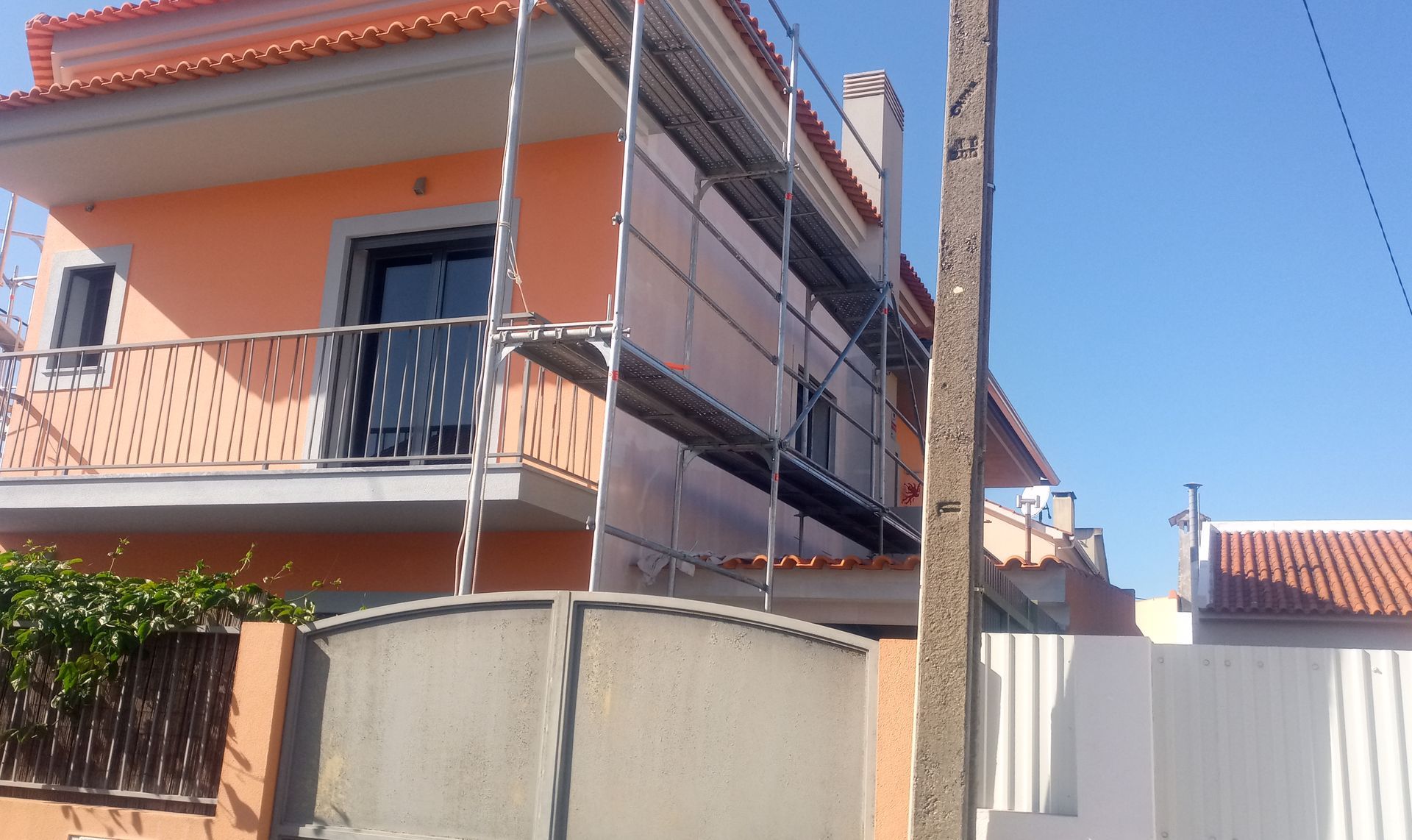 Prédio laranja com andaimes, cerca metálica e poste de energia.