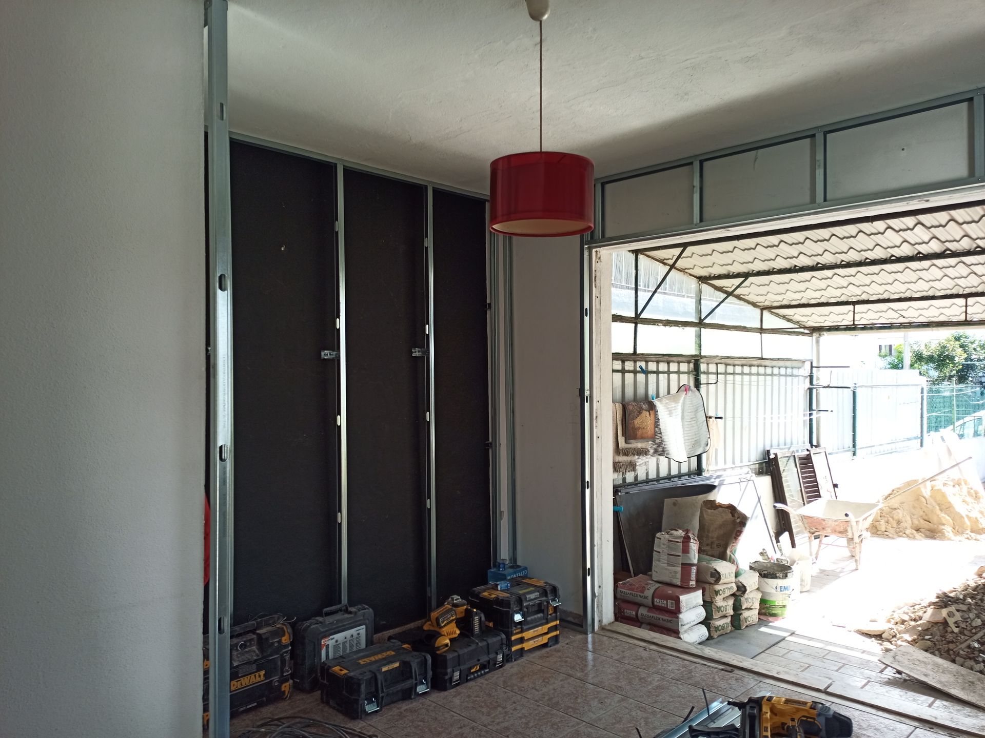 Vista interna de um cômodo em construção com estrutura aparente, isolamento e porta da garagem.