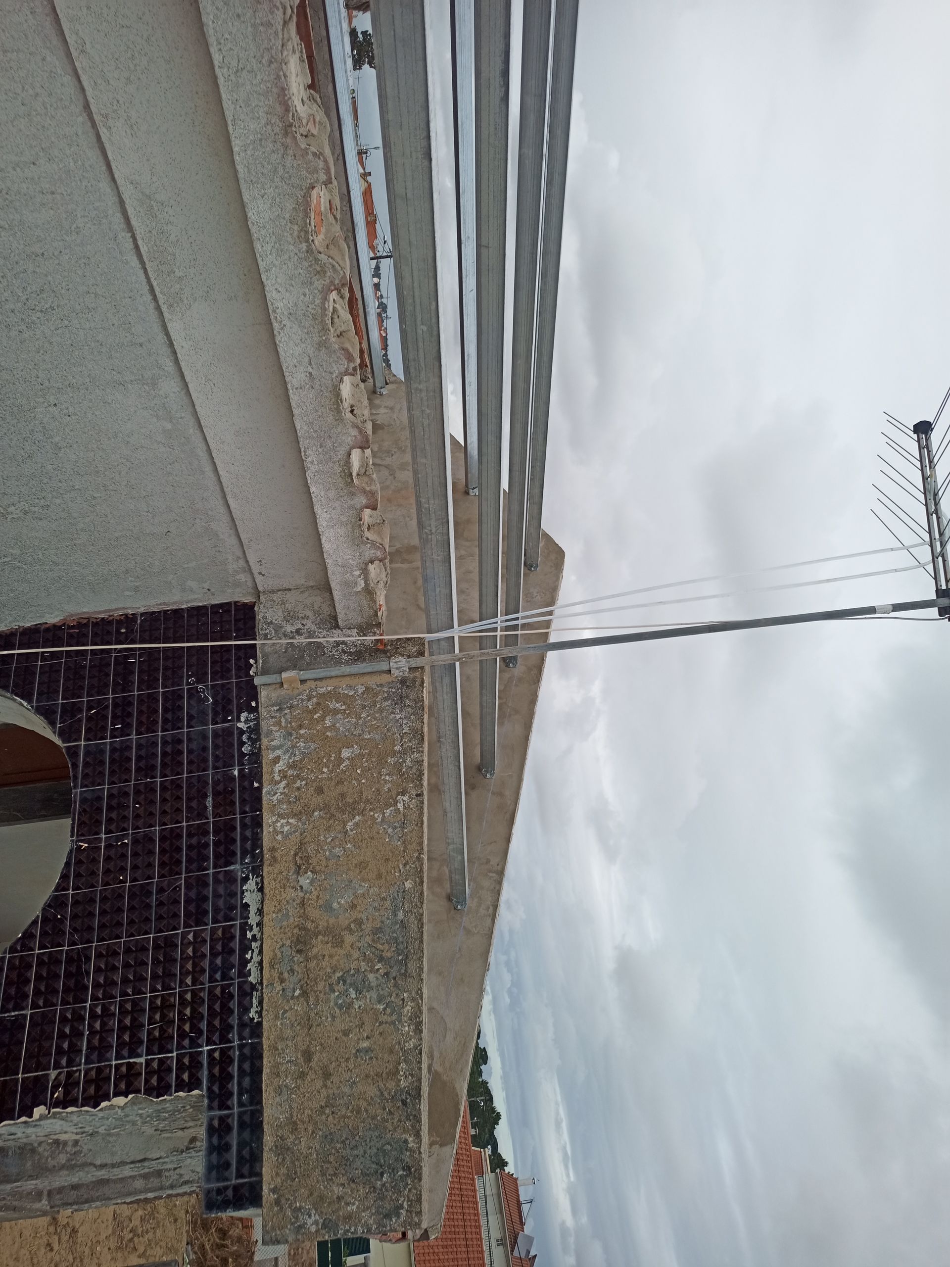 Borda do telhado com cobertura de metal ondulado, tijolos aparentes e céu nublado.