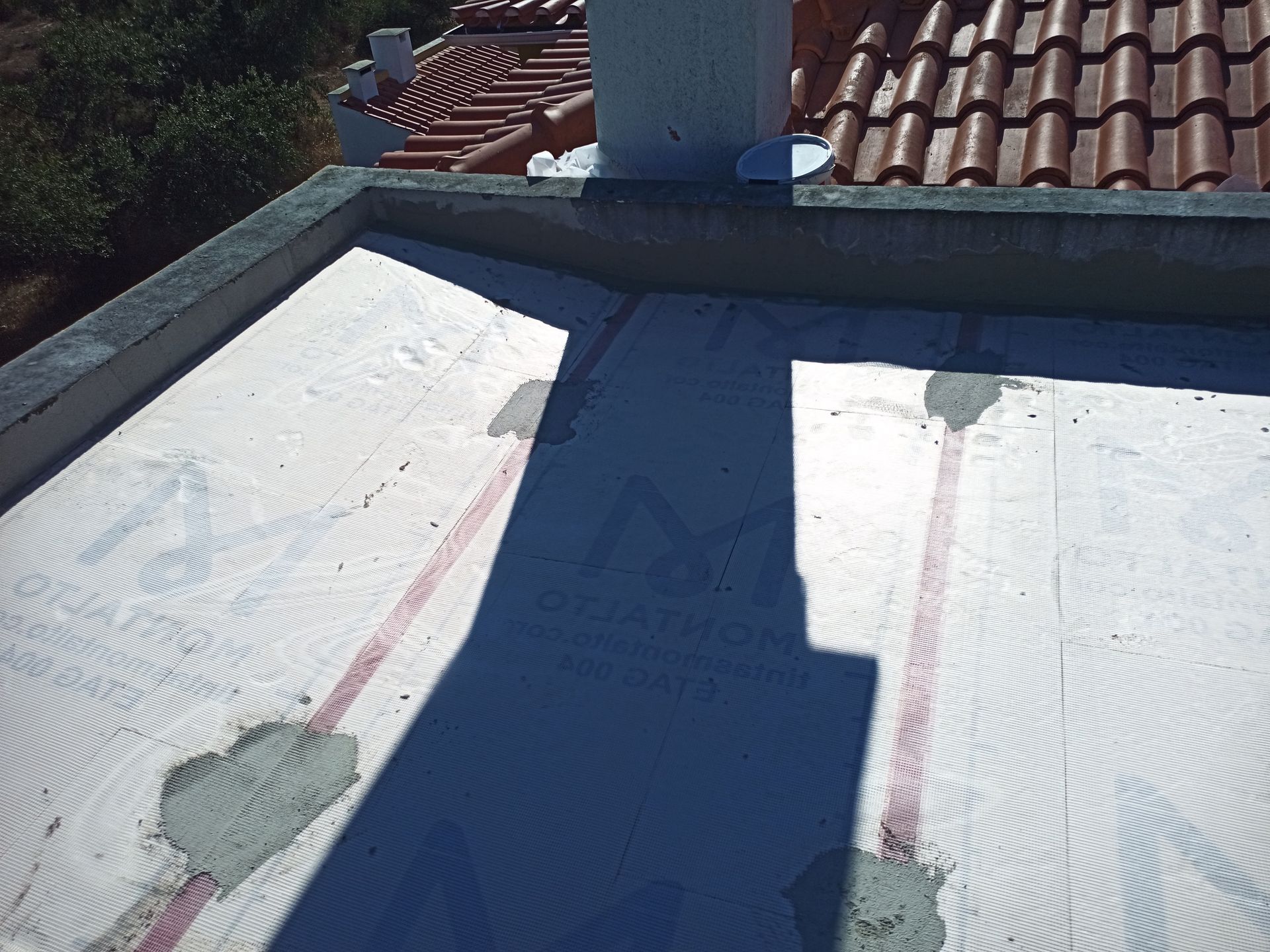 Telhado plano com cobertura branca, borda de concreto e chaminé.