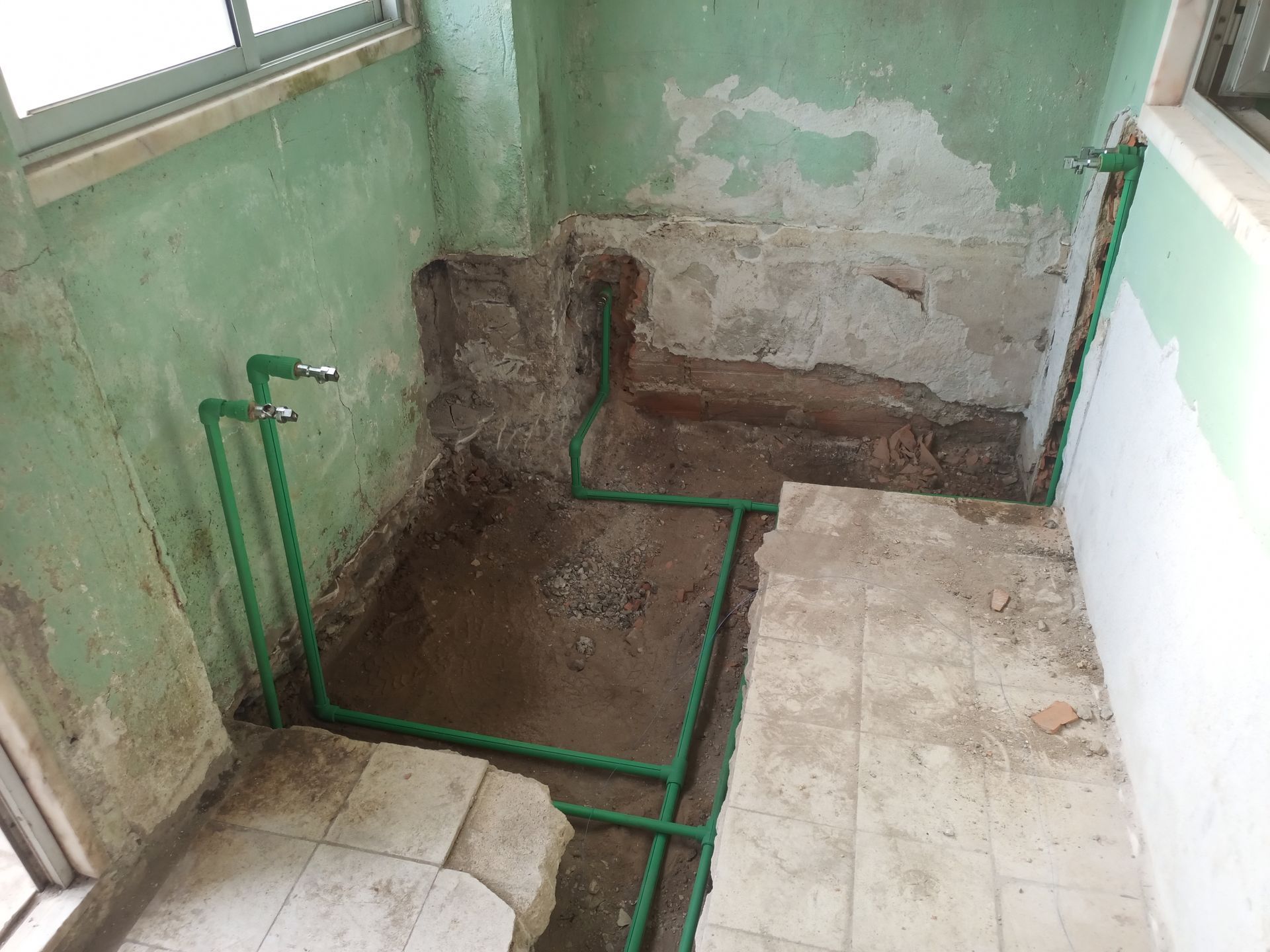 Tubulações verdes instaladas em um banheiro parcialmente demolido. Paredes verdes e azulejos cinza.