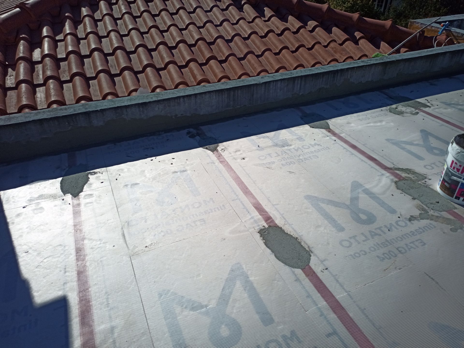 Telhado em construção com painéis isolantes e telhas vermelhas ao fundo.