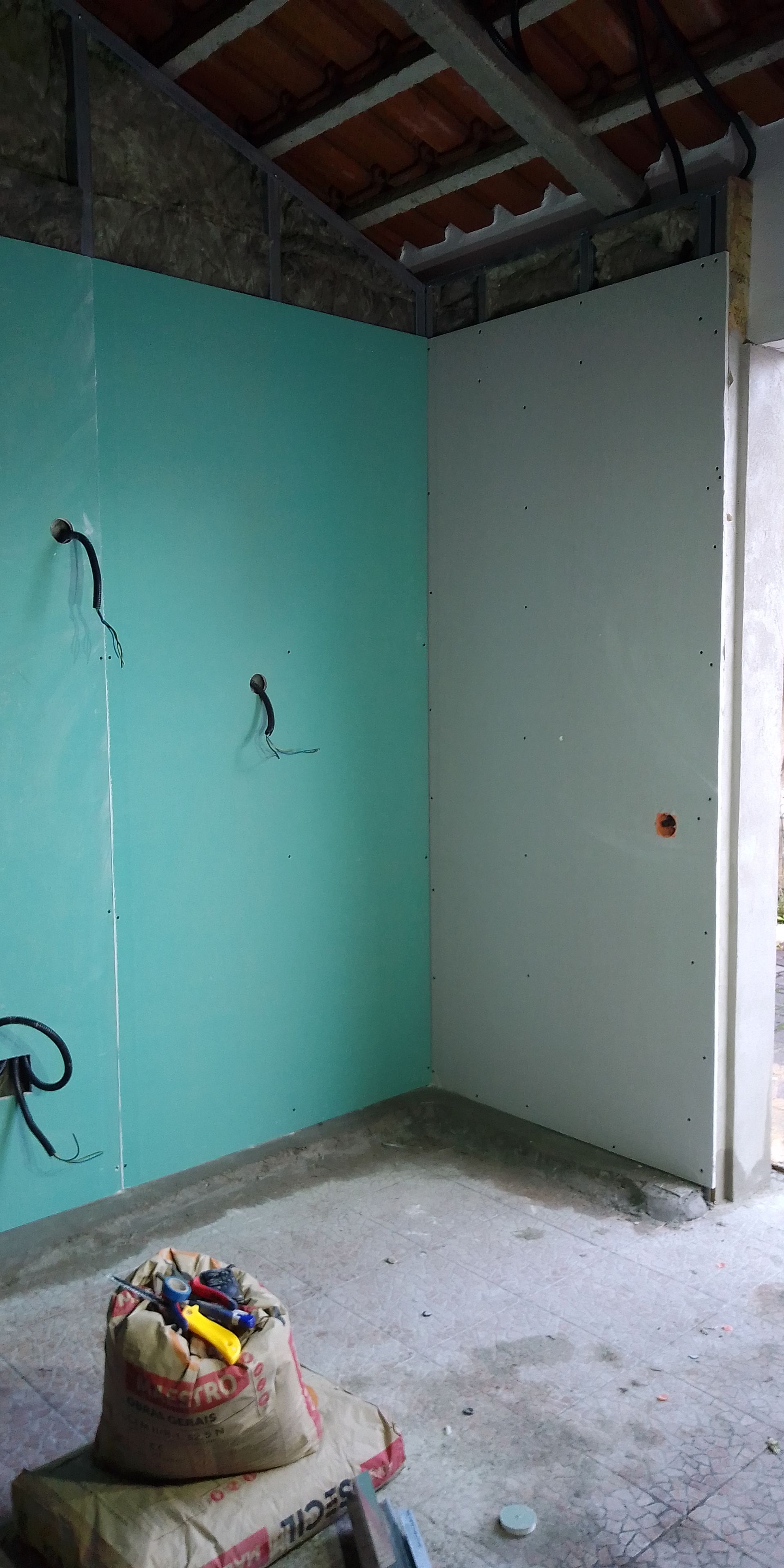 Canto interno de um cômodo em construção com drywall verde e branco e fiação exposta.