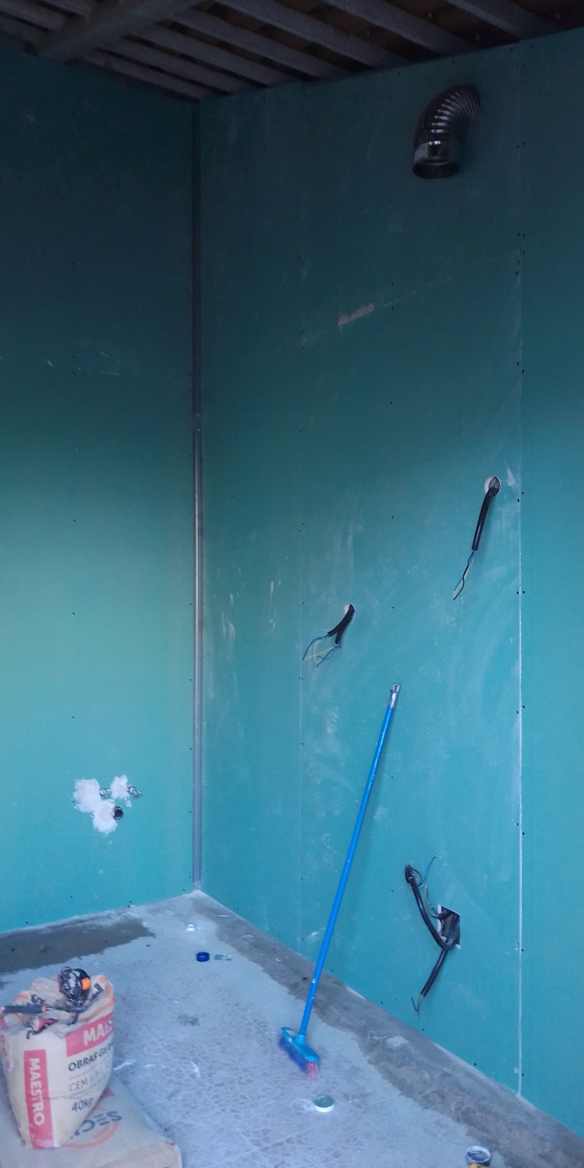Construção interior: Paredes azuis com instalações elétricas e hidráulicas, um saco de material e uma vassoura azul.