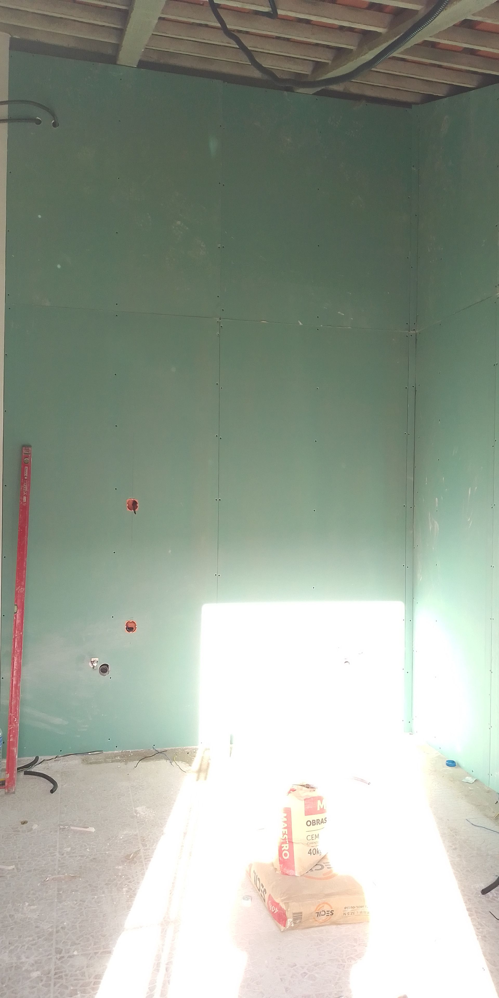 Canteiro de obras interno com paredes verdes, porta iluminada e teto aparente.