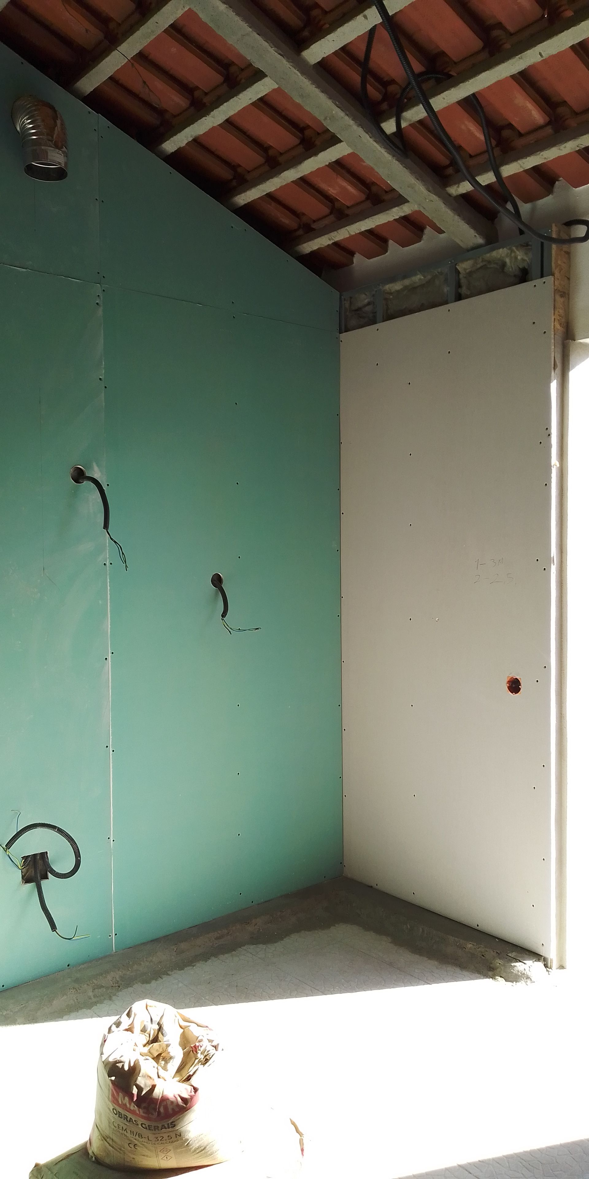 Canteiro de obras em ambiente interno, com paredes verdes e brancas e vigas de teto expostas.