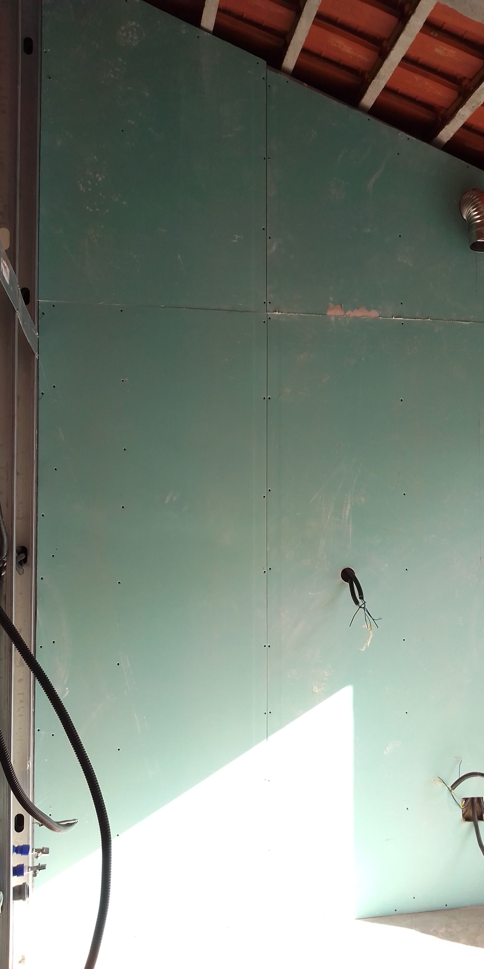 Painéis de gesso cartonado verde instalados contra um teto inclinado, sob um telhado de terracota.