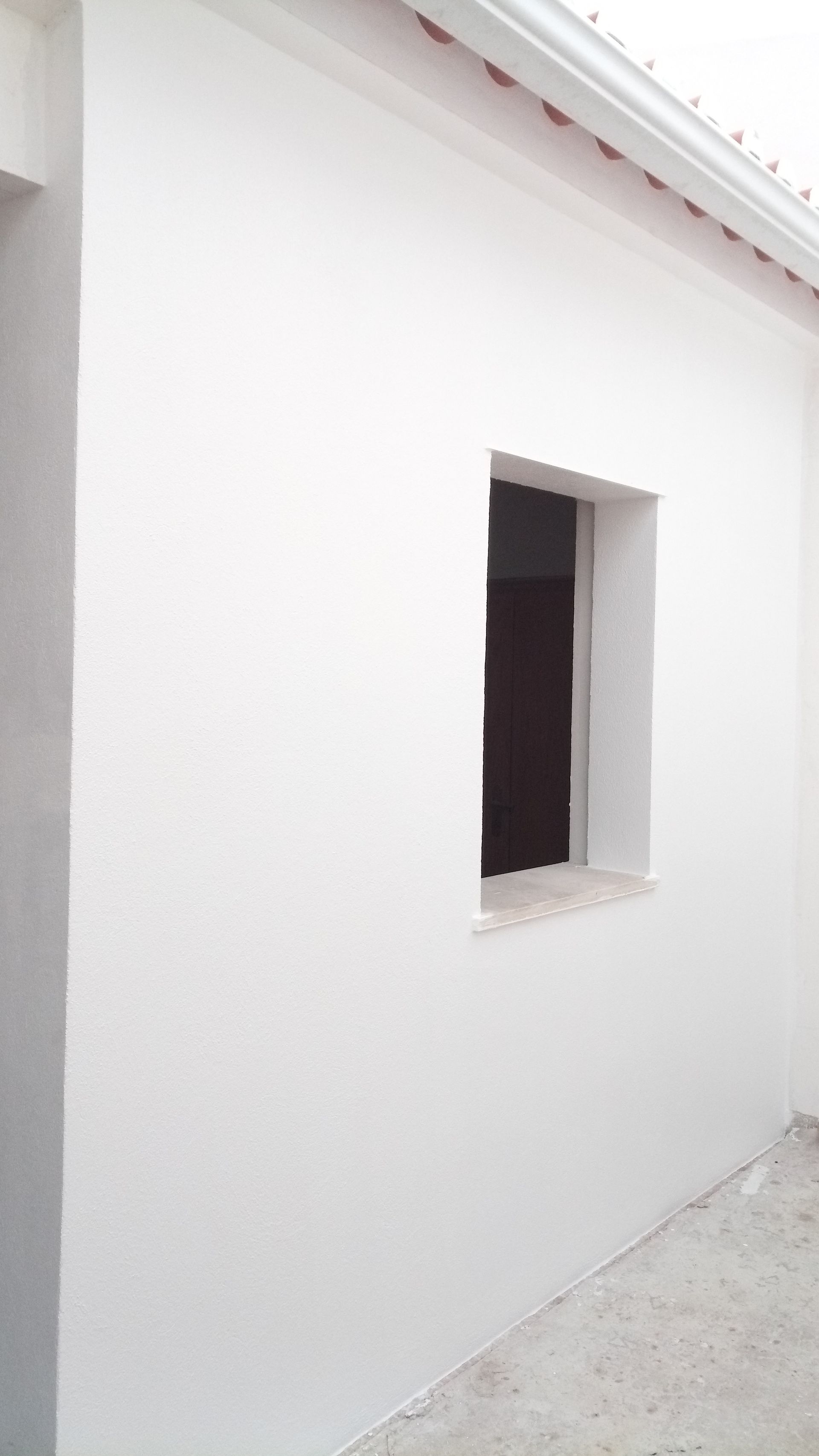 Exterior branco do prédio com uma pequena janela escura.