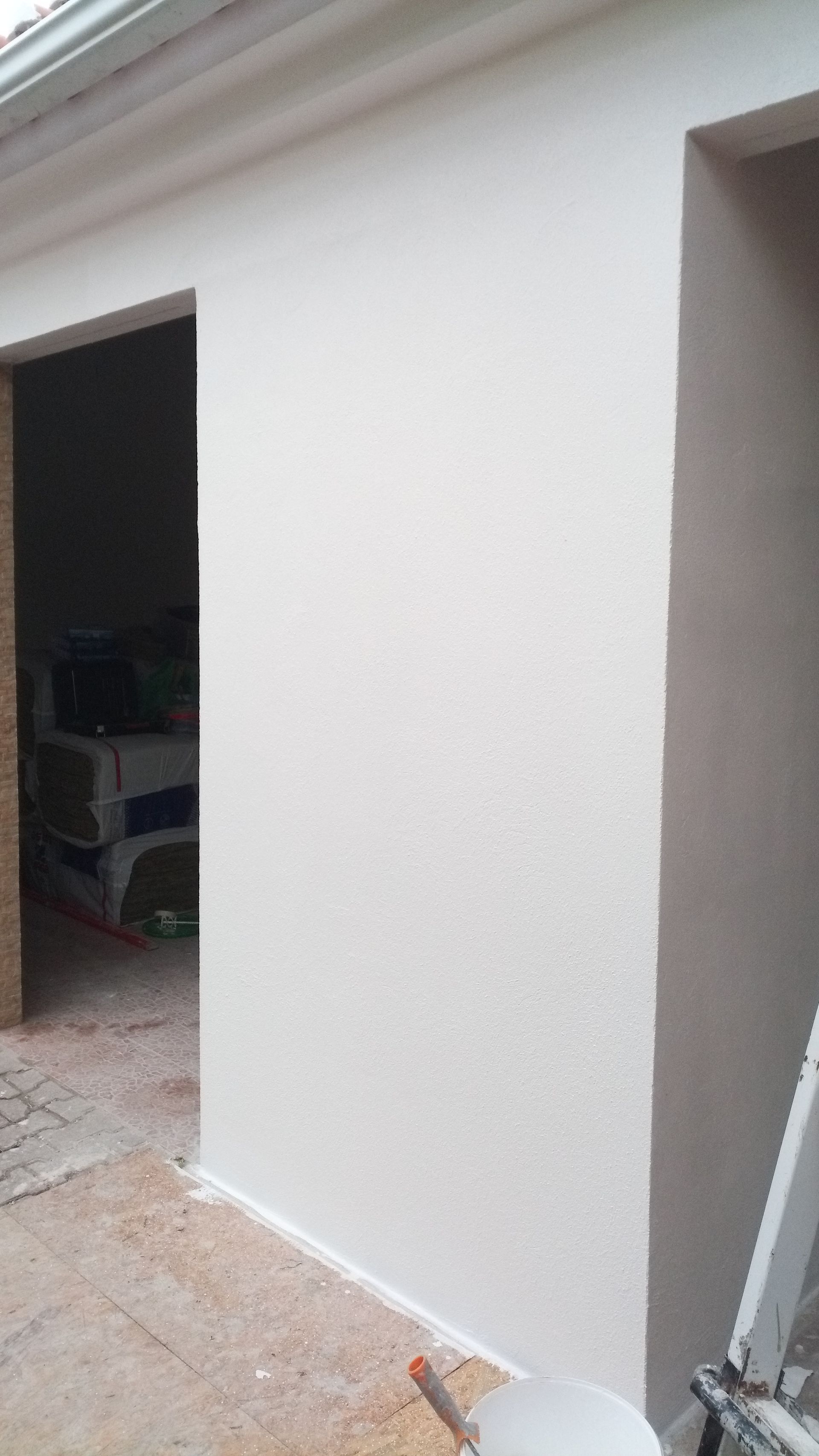 Parede branca texturizada com duas portas; piso marrom claro, objetos visíveis dentro das portas.