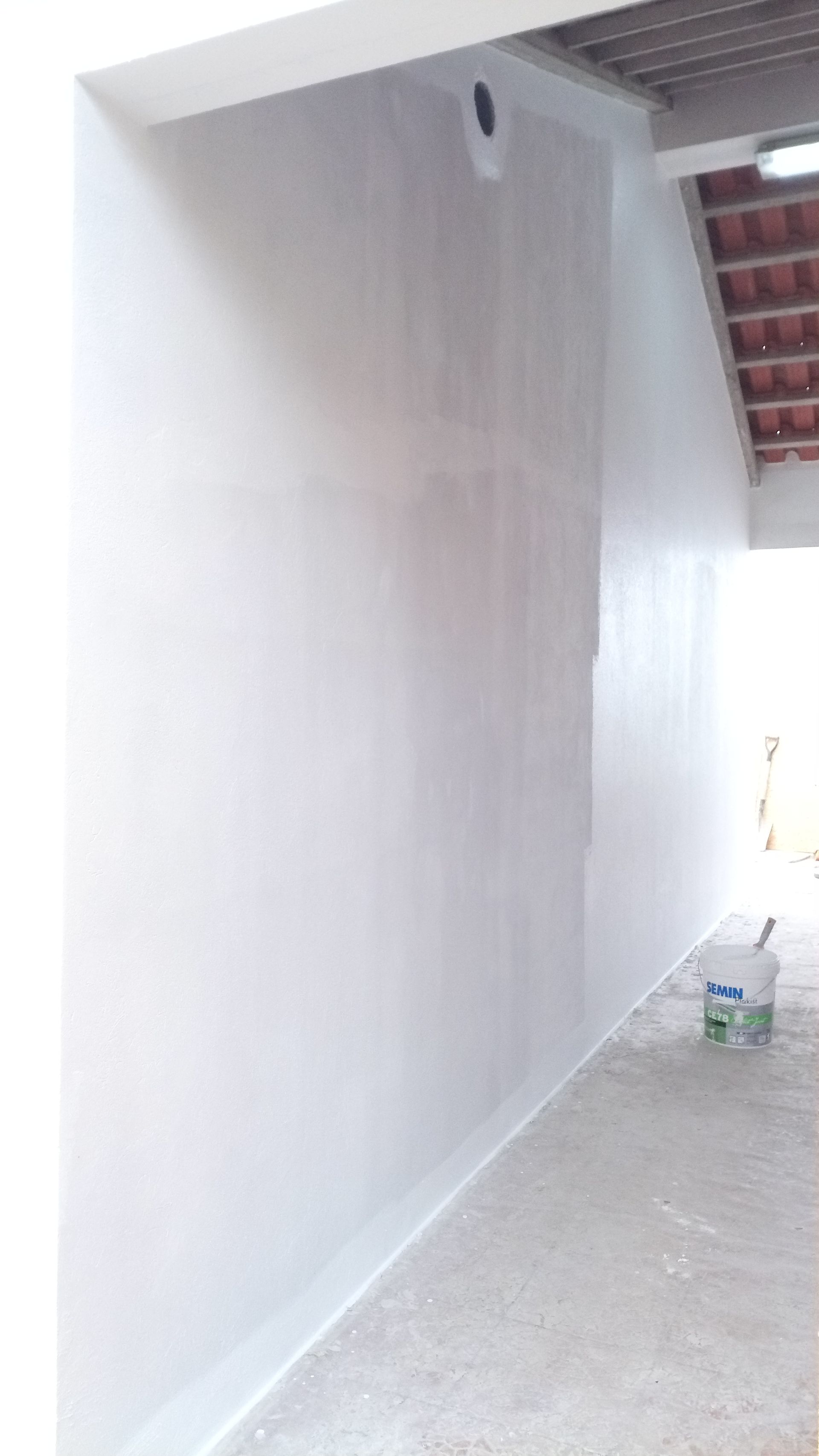 Parede pintada de branco com um balde sobre o chão de concreto ao lado de uma porta aberta.