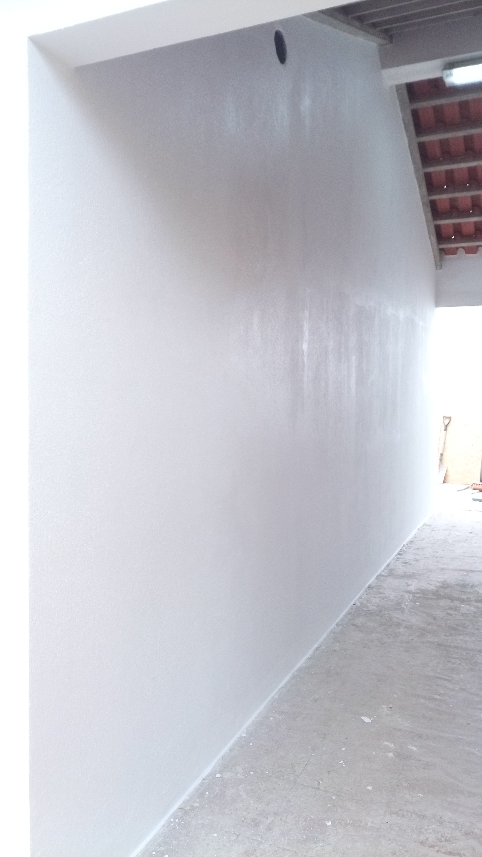 Parede pintada de branco com acabamento texturizado, vista de um canto, com vislumbre de um telhado aberto e passarela.