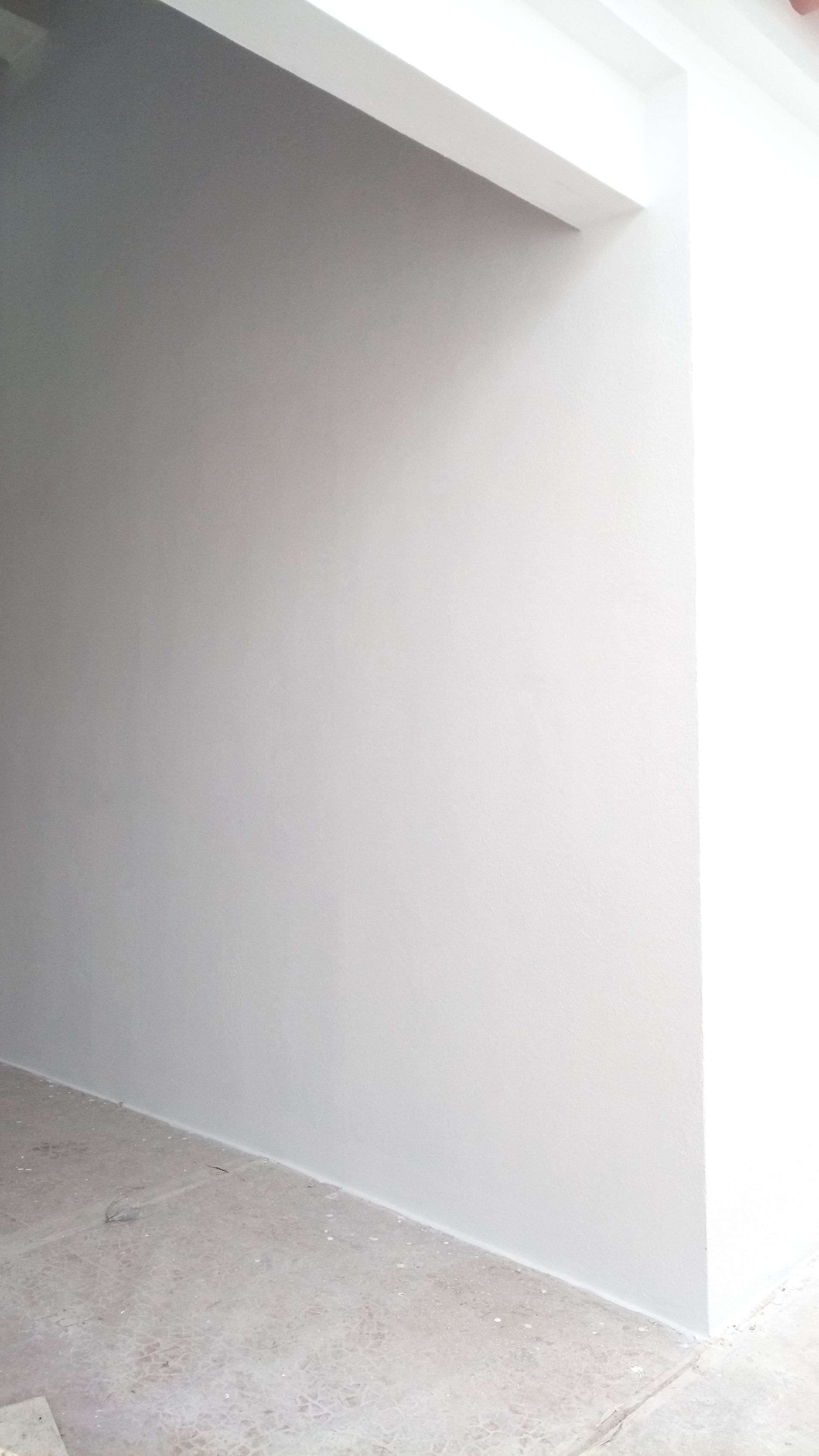 Paredes brancas em um quarto, com a luz do sol entrando por uma abertura no lado direito.