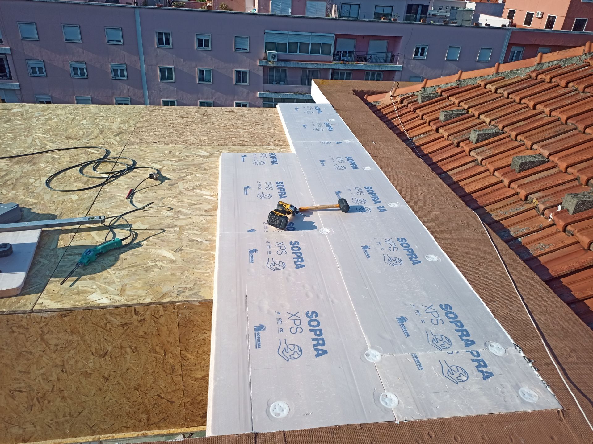 Instalação de isolamento de telhado com placas de espuma e ferramentas. Materiais nas cores marrom, laranja e branco.