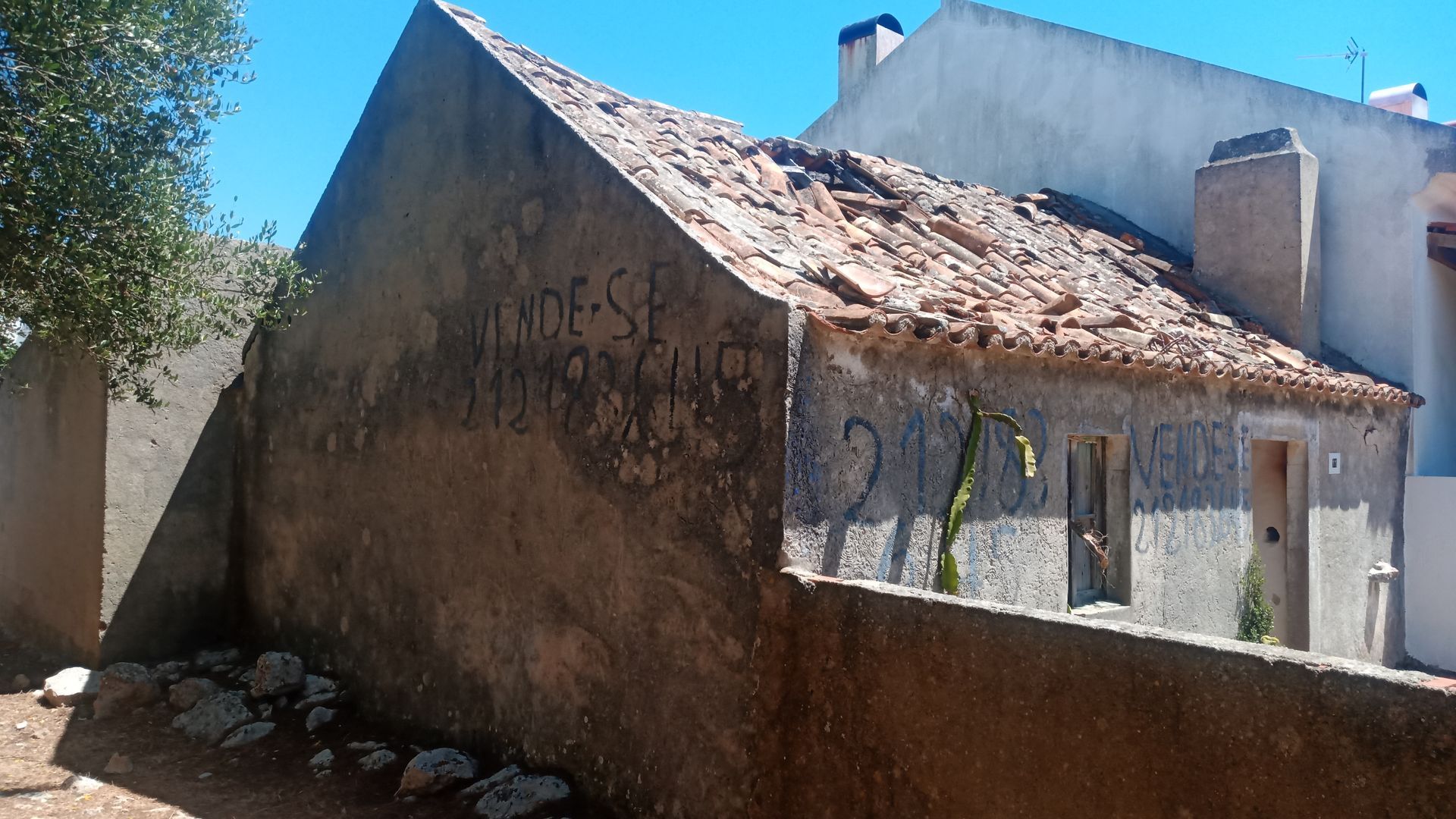 Prédio de concreto dilapidado com telhado de telhas quebrado, pichações e uma porta pequena.