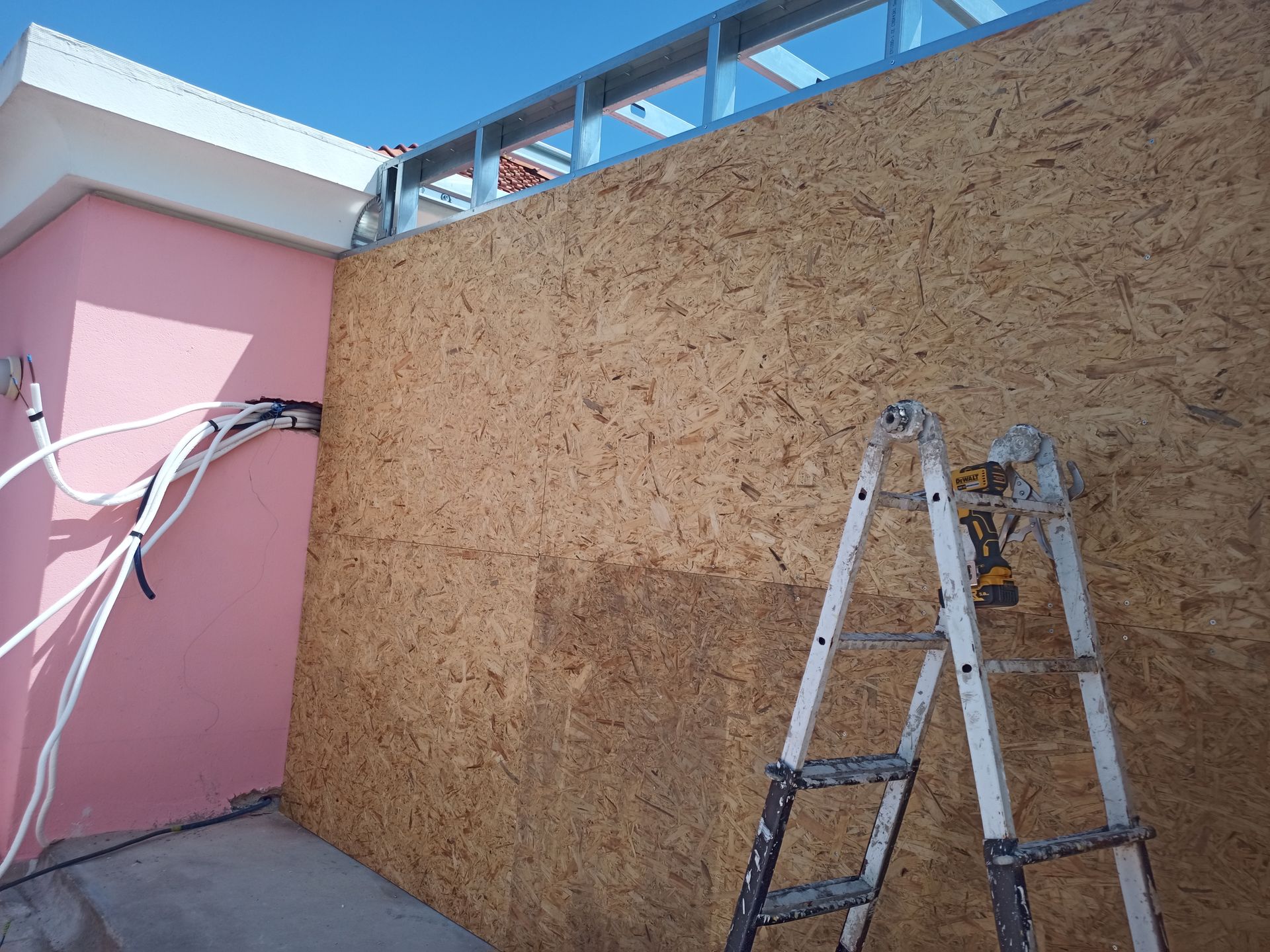 Canteiro de obras: painéis de OSB, parede pintada de rosa, estrutura metálica, escada e conduítes elétricos.